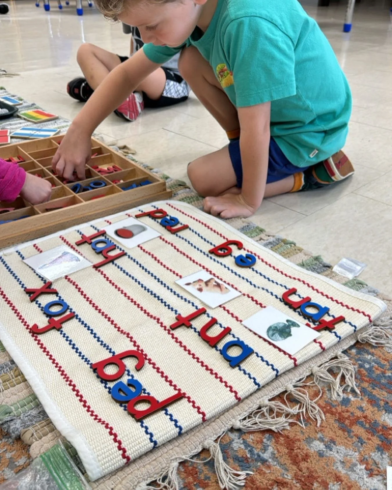 Child engaged in a Montessori-style activity, organizing alphabet letters on a striped mat with corresponding picture cards, focused on language learning.