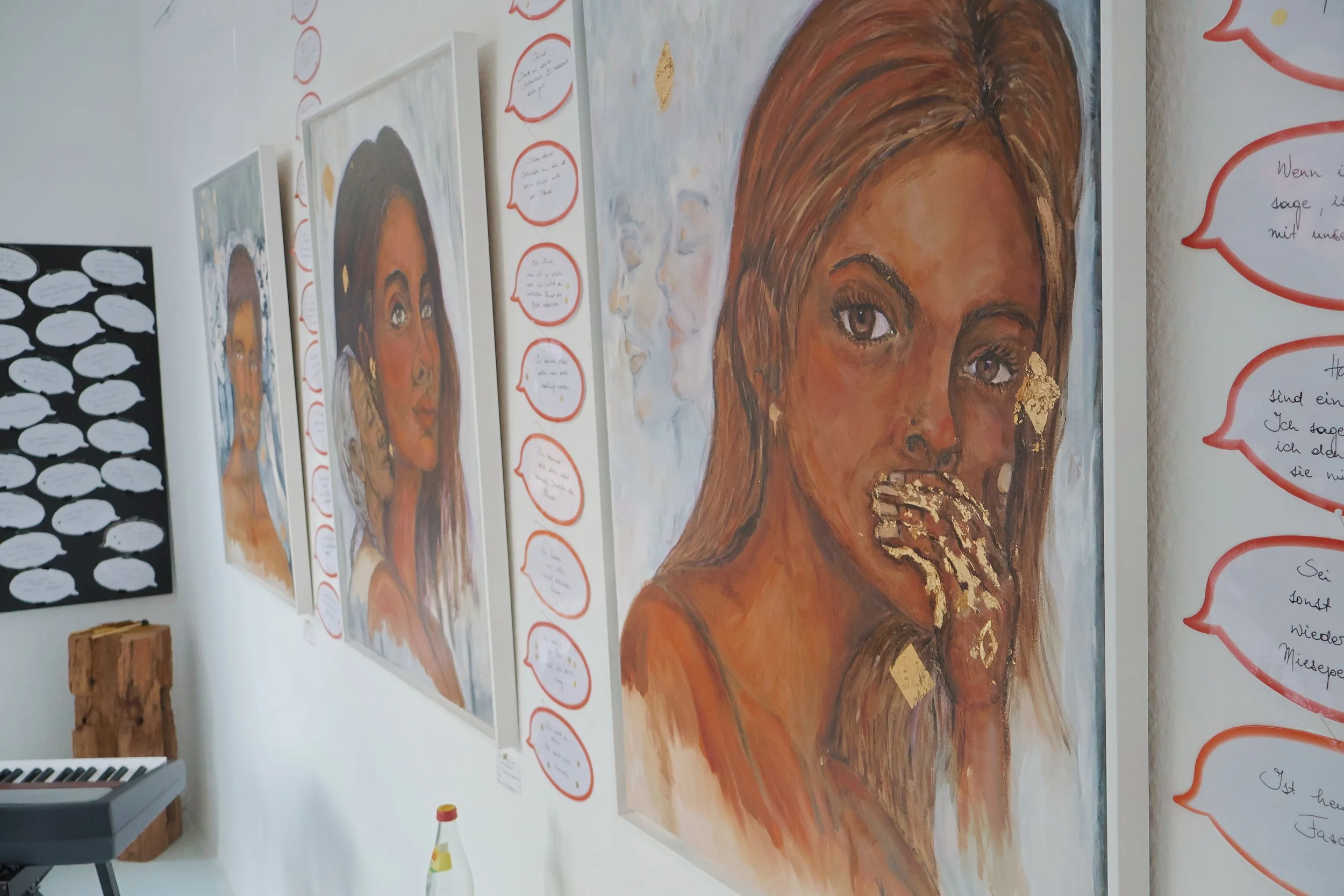 
Gemälde einer jungen Frau mit braunen Haaren und großen, ausdrucksvollen Augen und Goldakzenten, umgeben von roten Sprechblasen mit Texten, an der Wand in einem Raum. Ausstellung von Sonia Gonze in der Roten Galerie Nürnberg.