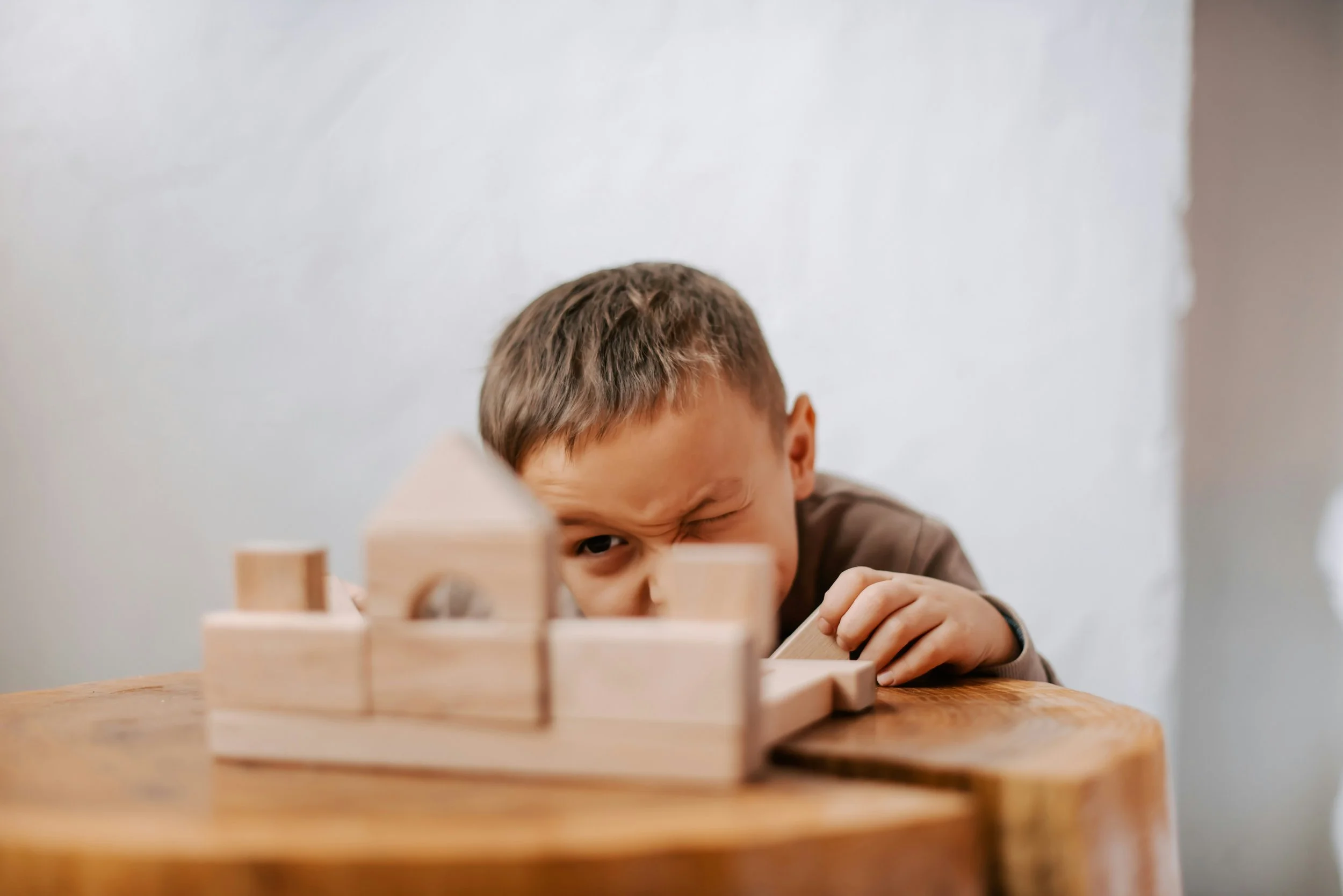 Een jongen speelt met houten blokken op een tafel, met een witte muur op de achtergrond.