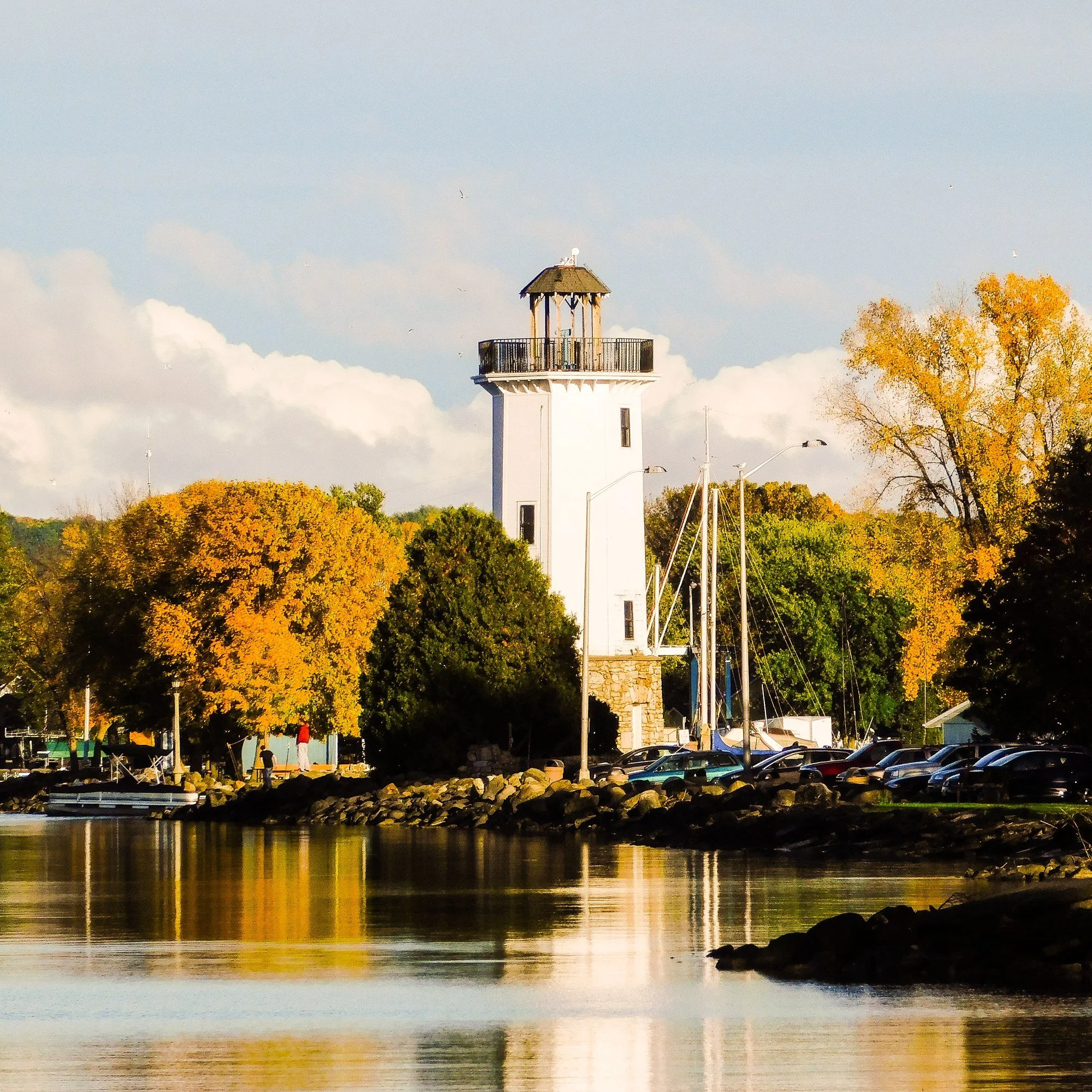The white lighthouse at Lakeside Park in Fond du Lac, Wisconsin, surrounded by fall trees and reflected in the water.
