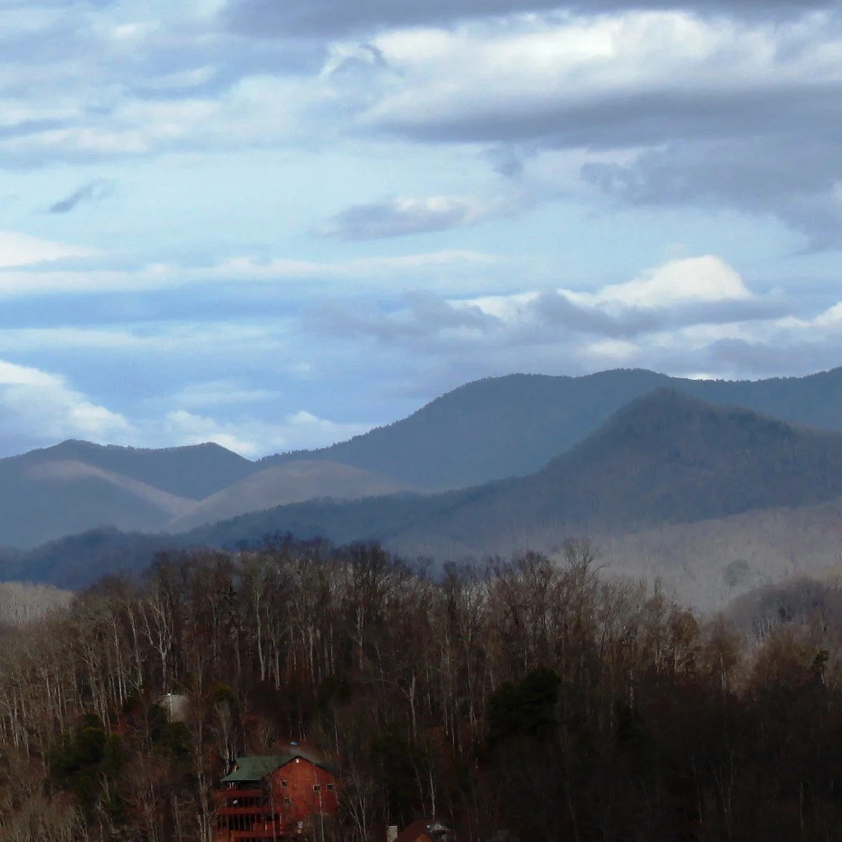 Mountain ridgelines near Whittier, North Carolina, under heavy clouds, with bare trees in the foreground.