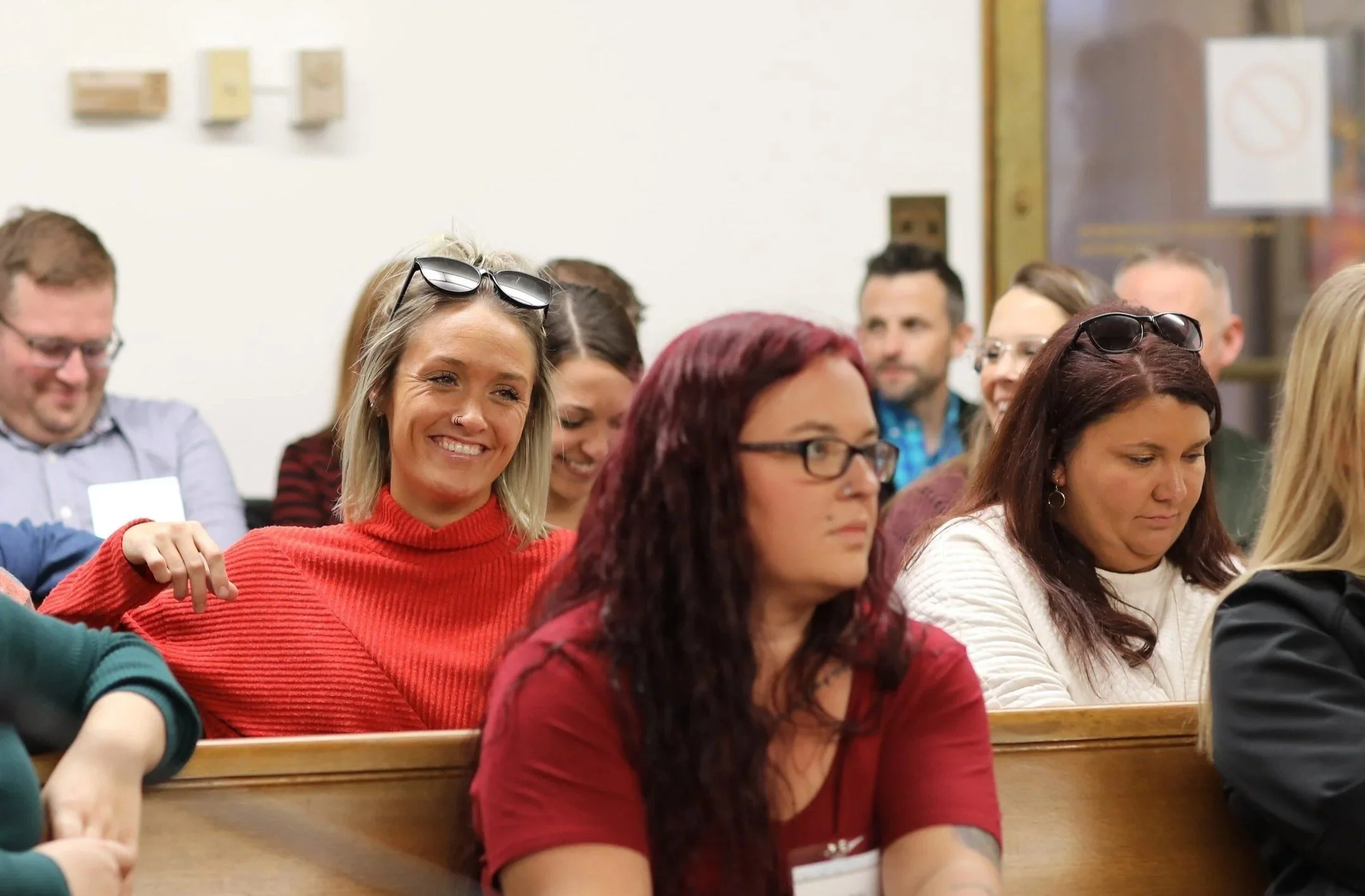 People sitting in a room attending a seminar or conference, some wearing glasses, some with sunglasses on their heads, smiling or looking serious.