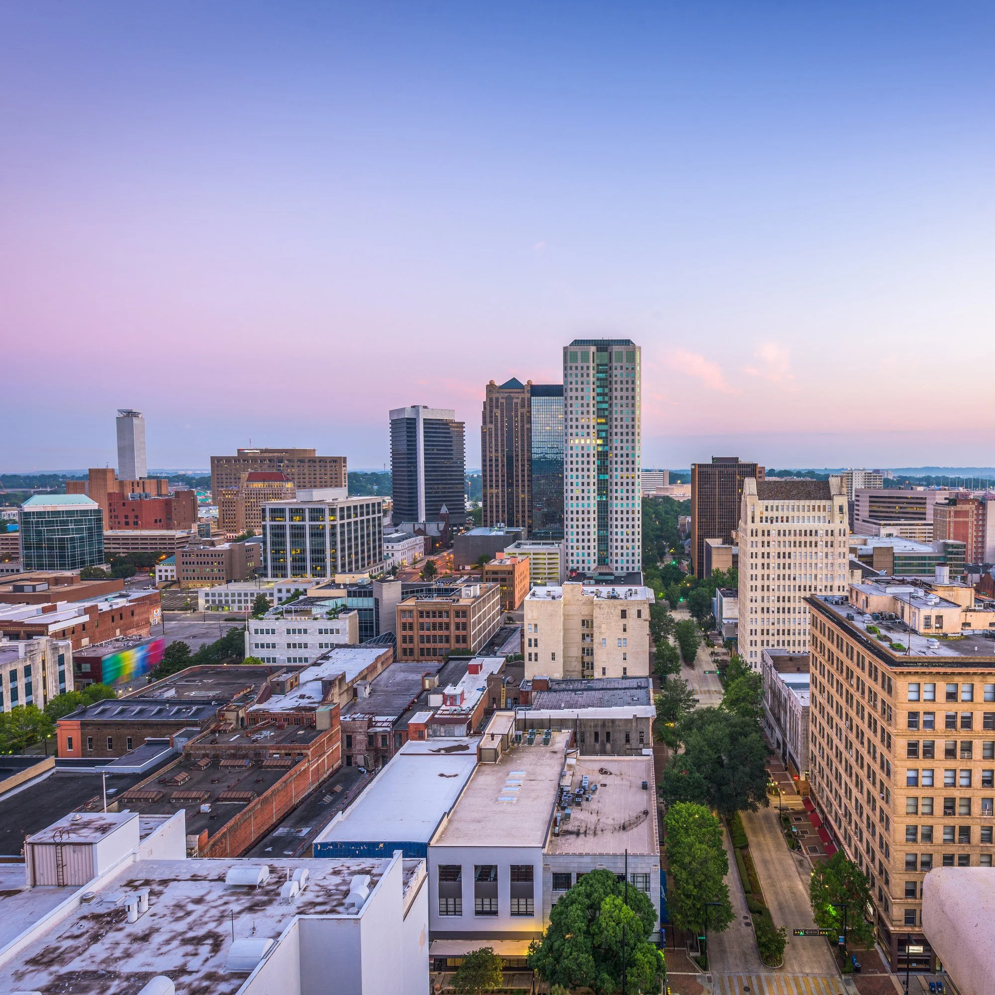Downtown Birmingham, Alabama, at dusk, seen from a historic rooftop with a carved stone figure in the foreground.
