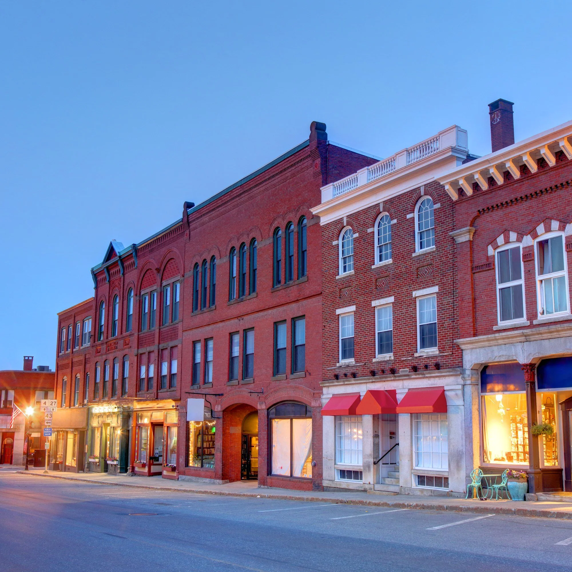 Brick storefronts along a street in downtown Farmington, Maine, at dusk.