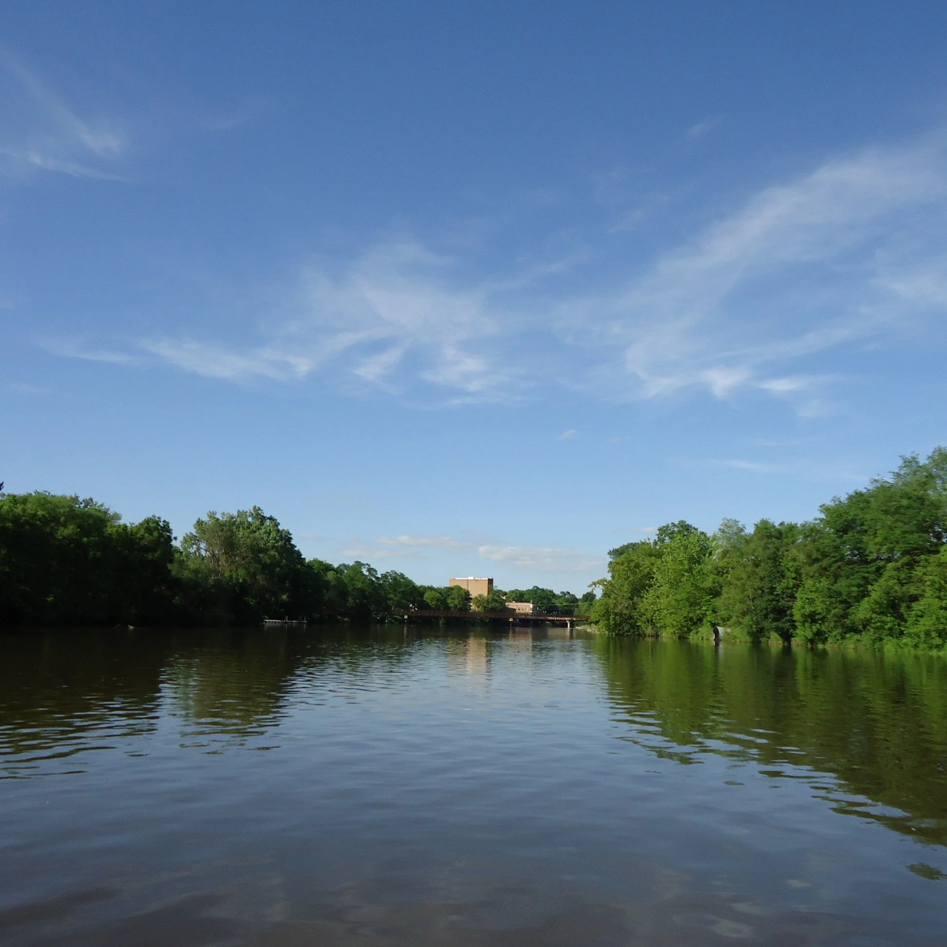 The Kishwaukee River, lined with green trees under a blue sky.