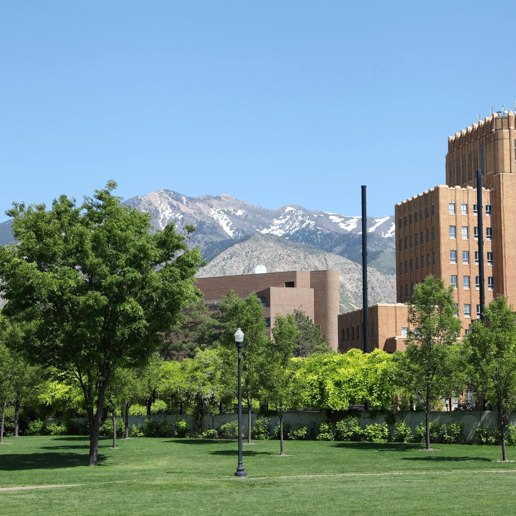 A park and historic buildings in downtown Ogden, Utah, with snow-capped mountains behind.