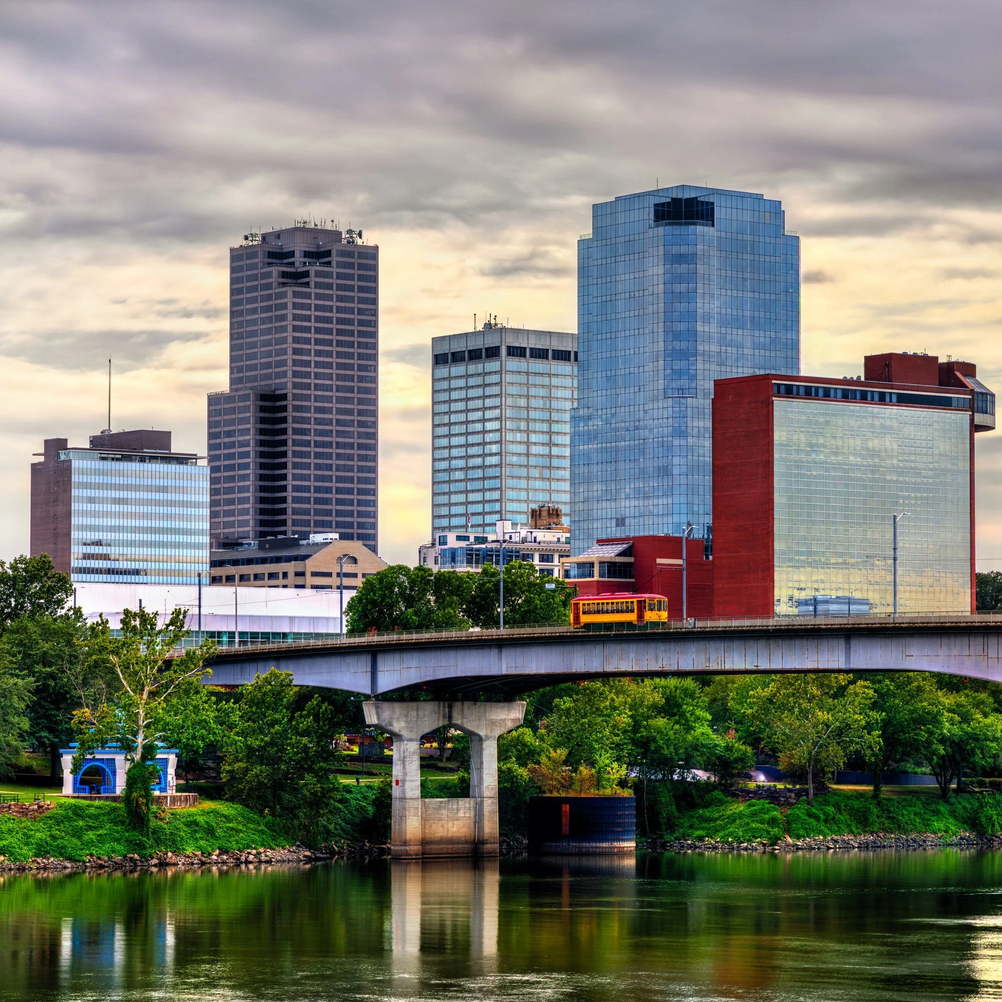 The downtown Little Rock, Arkansas, skyline above the Arkansas River, with a streetcar crossing the Main Street Bridge.