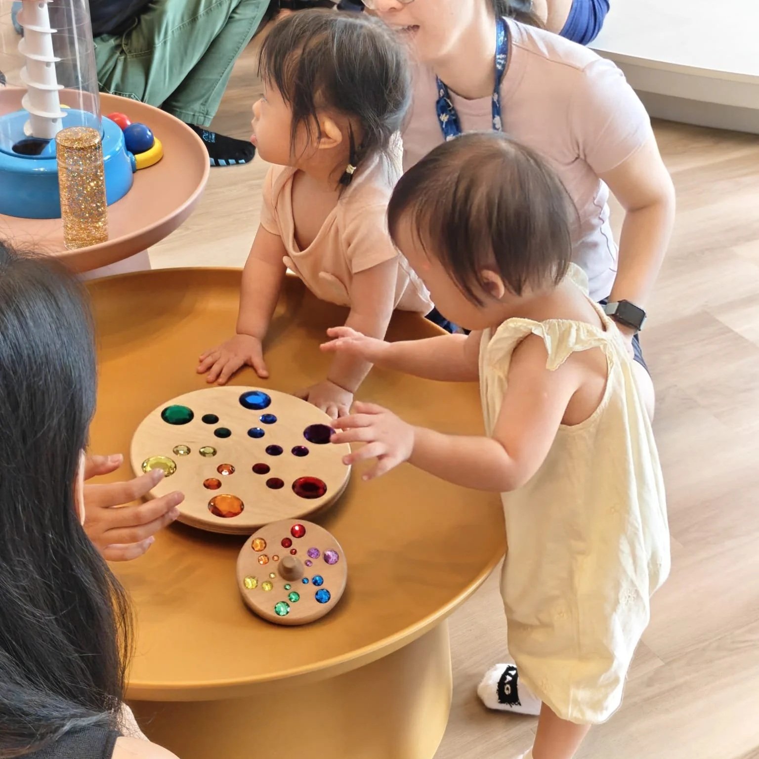 Children and an adult playing with colorful gemstone and jewel discovery game on a wooden table in a classroom or playroom.