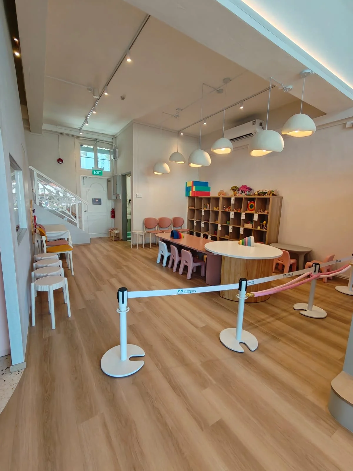 Empty children's play area with pastel chairs, toys, and a wooden shelf, cordoned off with a pink barrier.