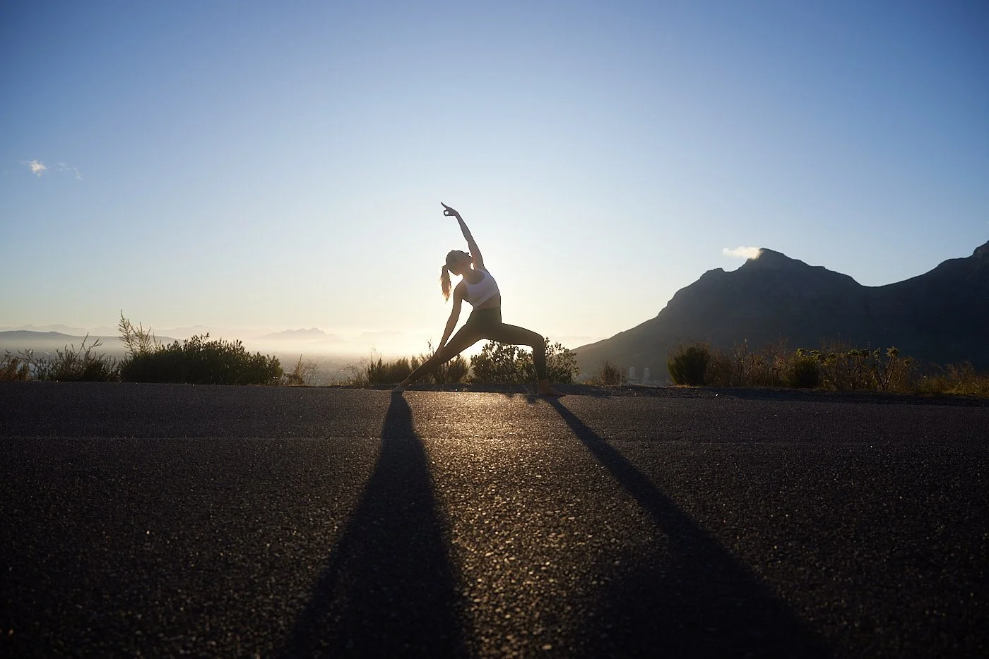 Silhouette einer Person, die Yoga im Freien bei Sonnenuntergang vor einer Bergkulisse praktiziert.