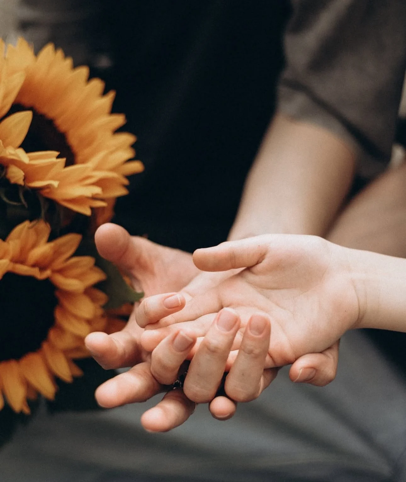 Hands holding with a bouquet of sunflowers in the background.