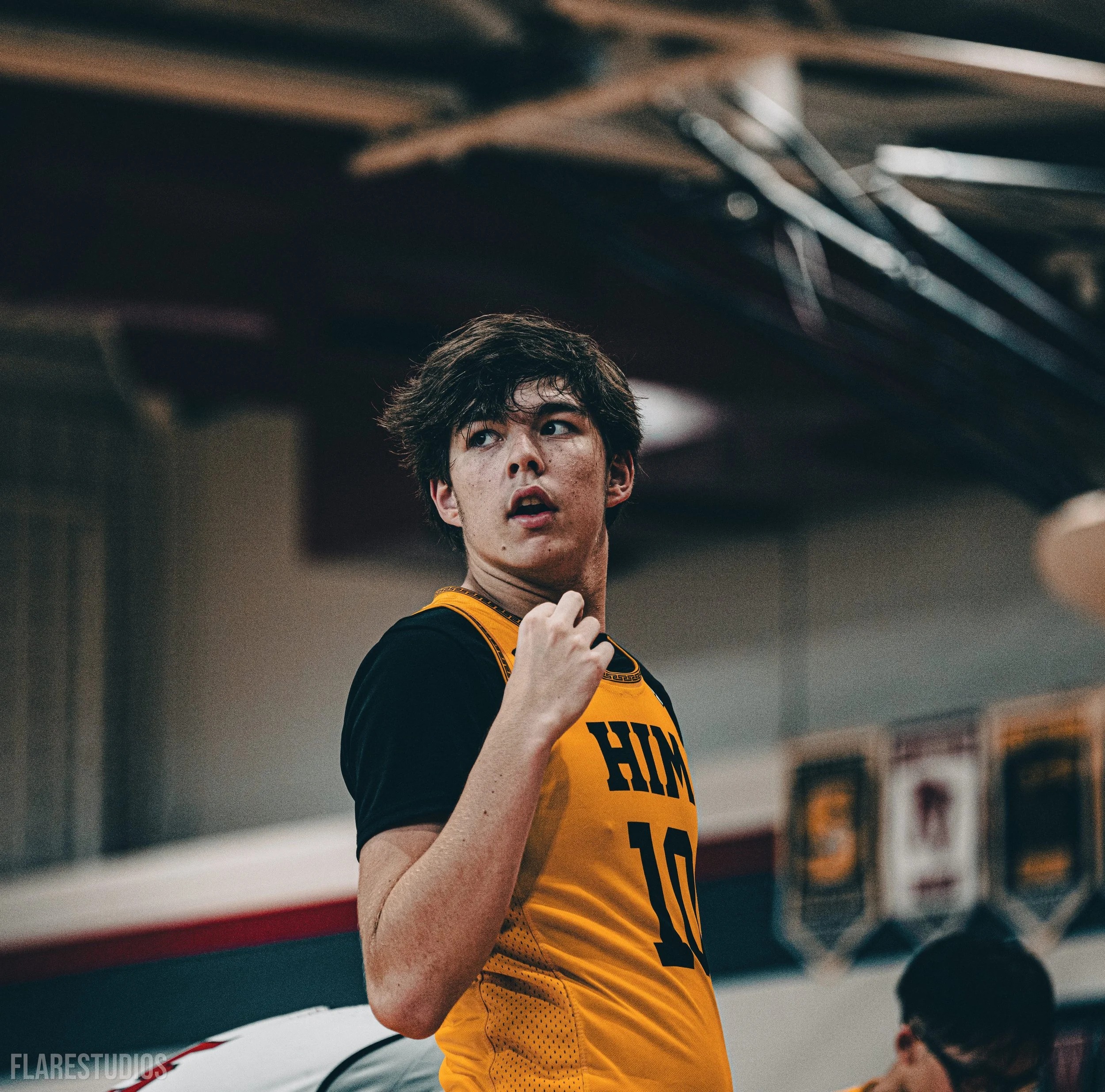 Young male athlete in a yellow sports jersey with black accents, number 10, looking to the side in a gym or sports facility.