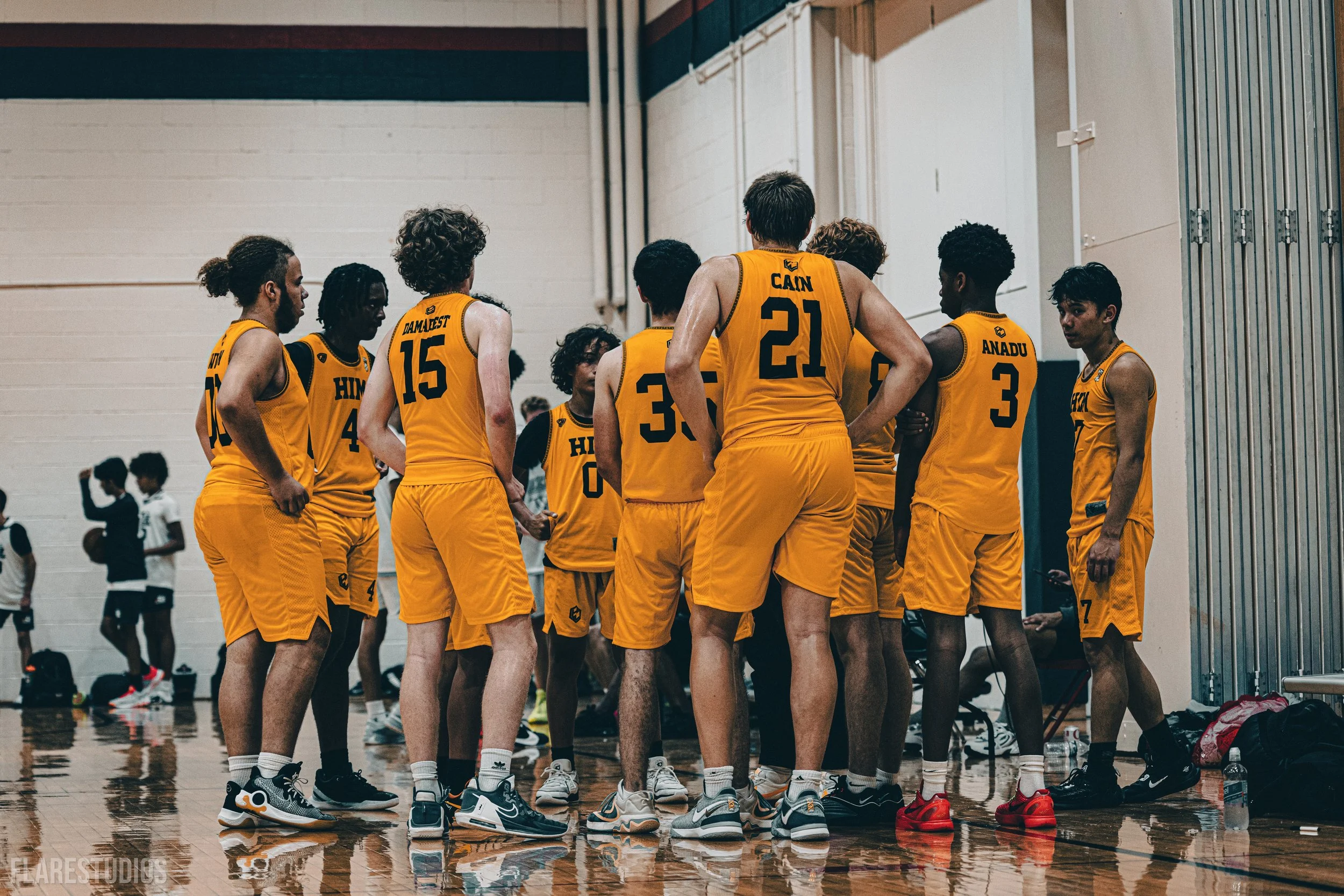 A group of basketball players in yellow uniforms gathered in a huddle on an indoor basketball court.