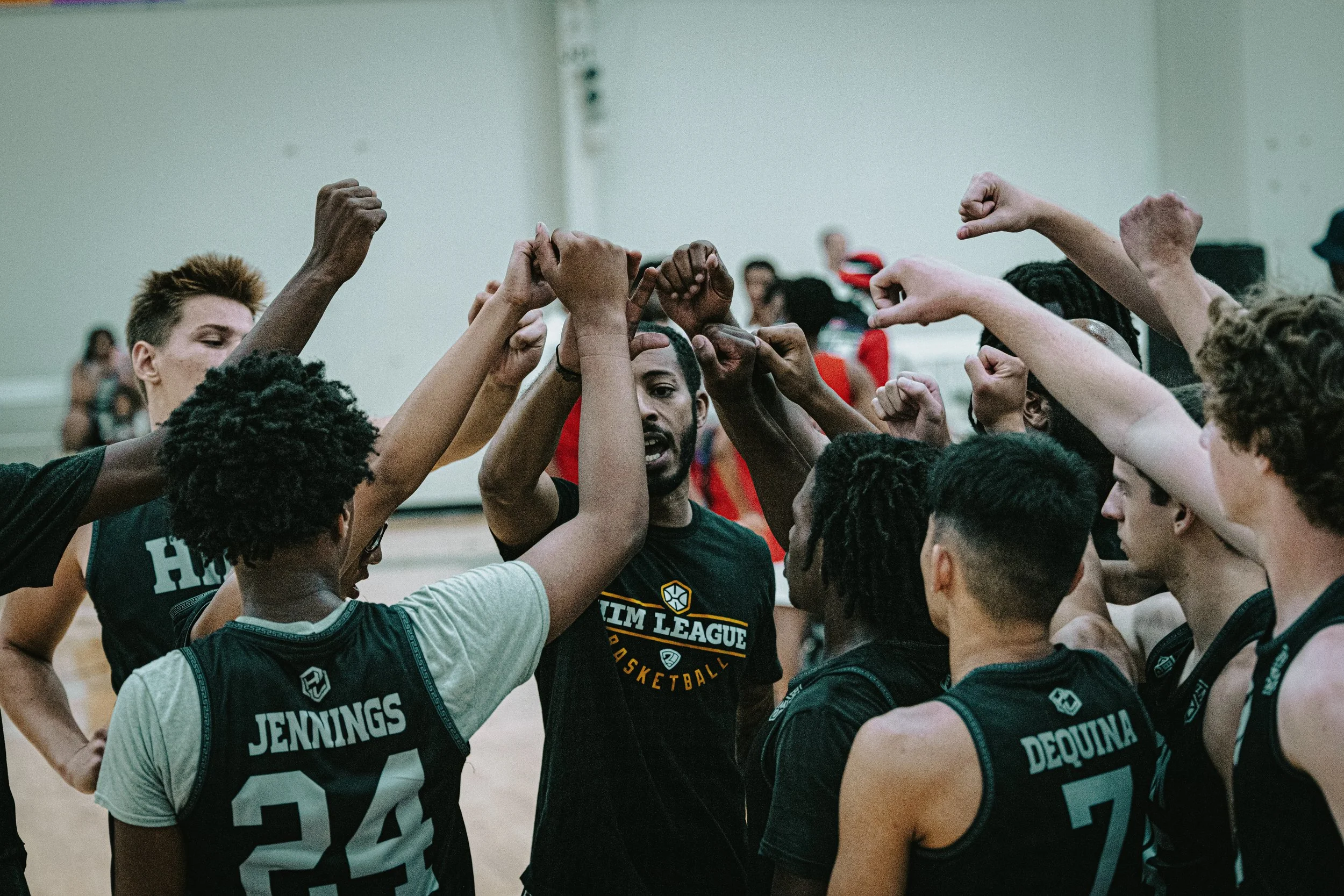 A diverse group of basketball players huddles together with their hands raised in a team cheer during a game or practice.