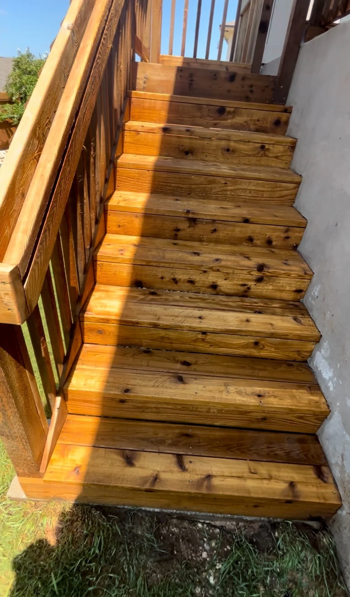 Wooden outdoor stairs with railing leading to an elevated doorway, with sunlight casting shadows on the steps.