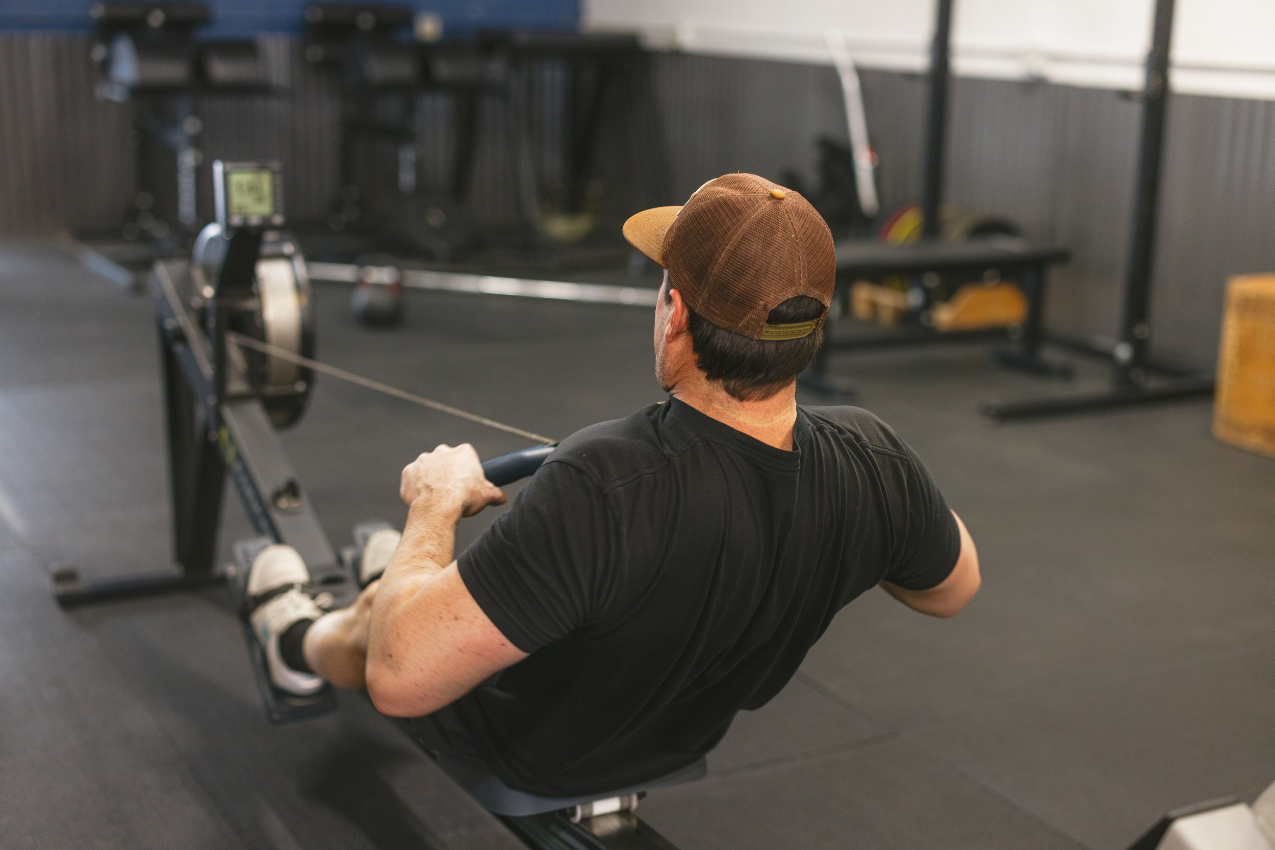 Man in a cap using a rowing machine in a gym.