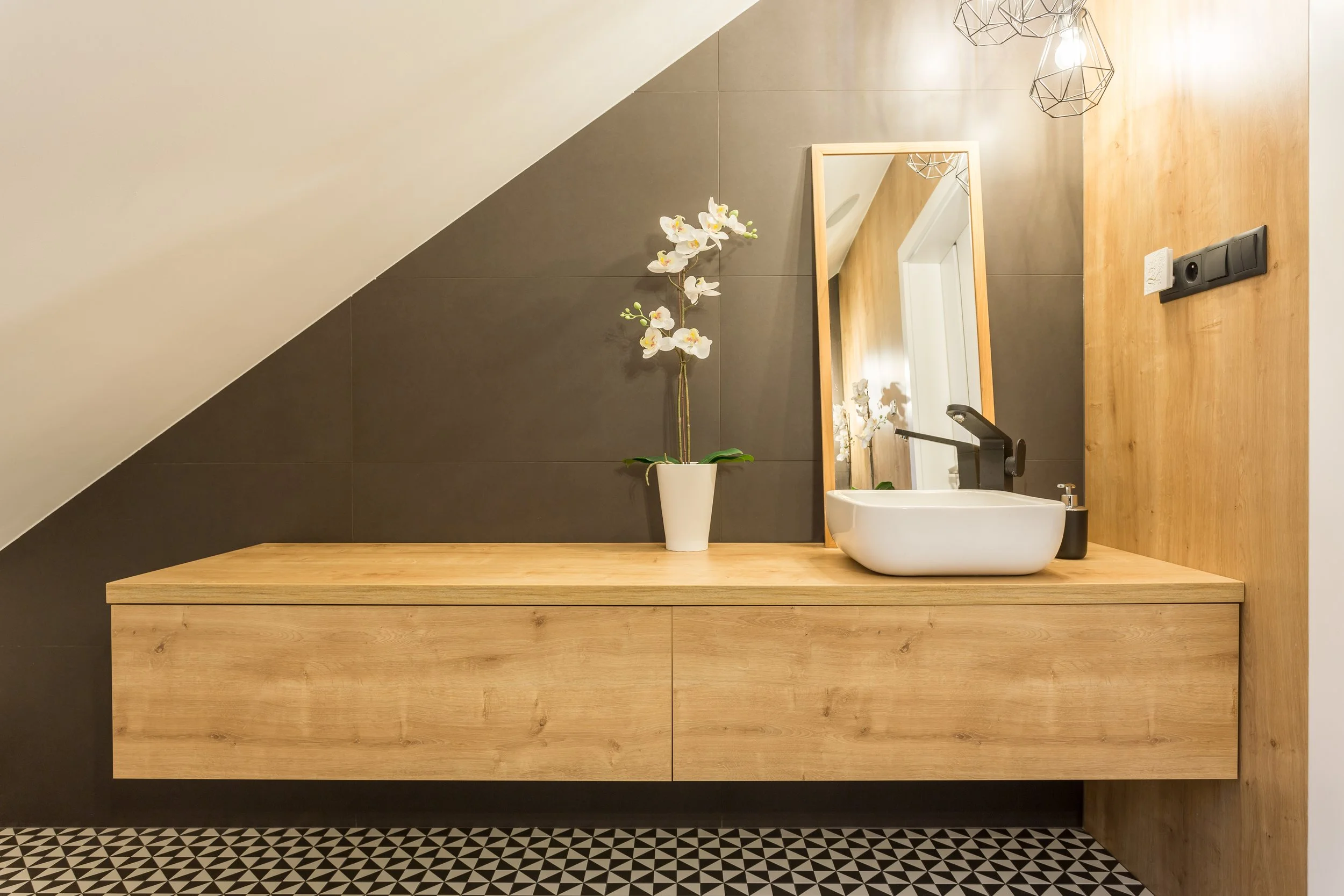 Lavabo de salle de bain moderne avec un miroir, une plante orchidée blanche en pot, et un robinet noir, avec un mur en bois et un mur gris foncé