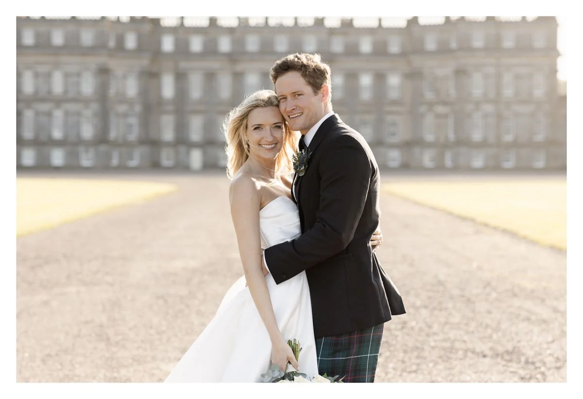 Happy bride and groom embracing at the front of the stunning Hopetoun House, South Queensferry on a beautiful summers day