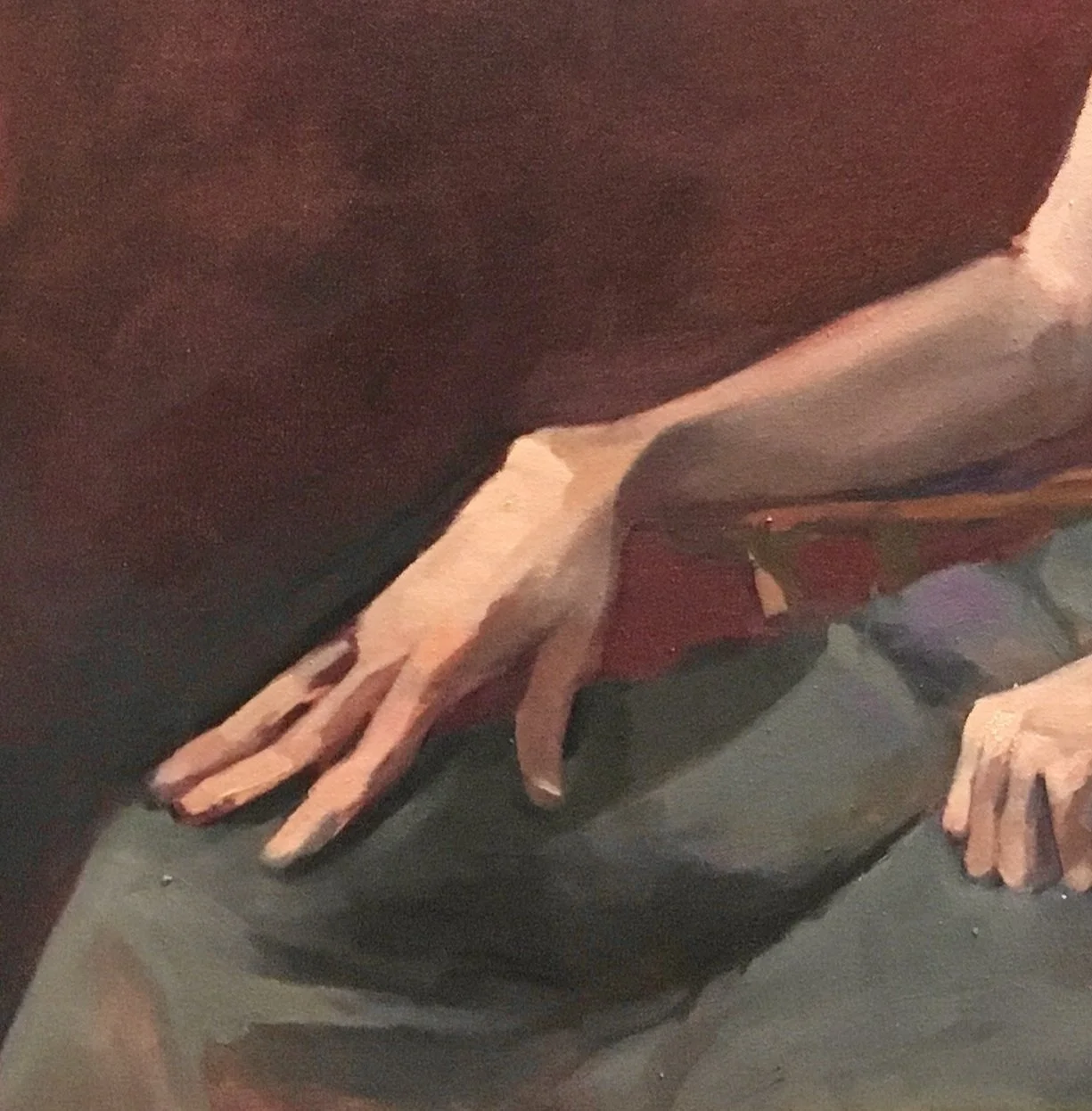 Part of a portrait. Zoom in on their left arm resting on their lap, wearing a dark short-sleeve shirt and dark pants.