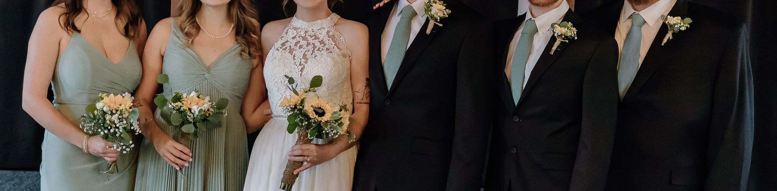 Group of wedding guests, including bridesmaids in light green dresses holding bouquets, and groomsmen in black suits with light green ties and boutonnieres, at a wedding celebration.
