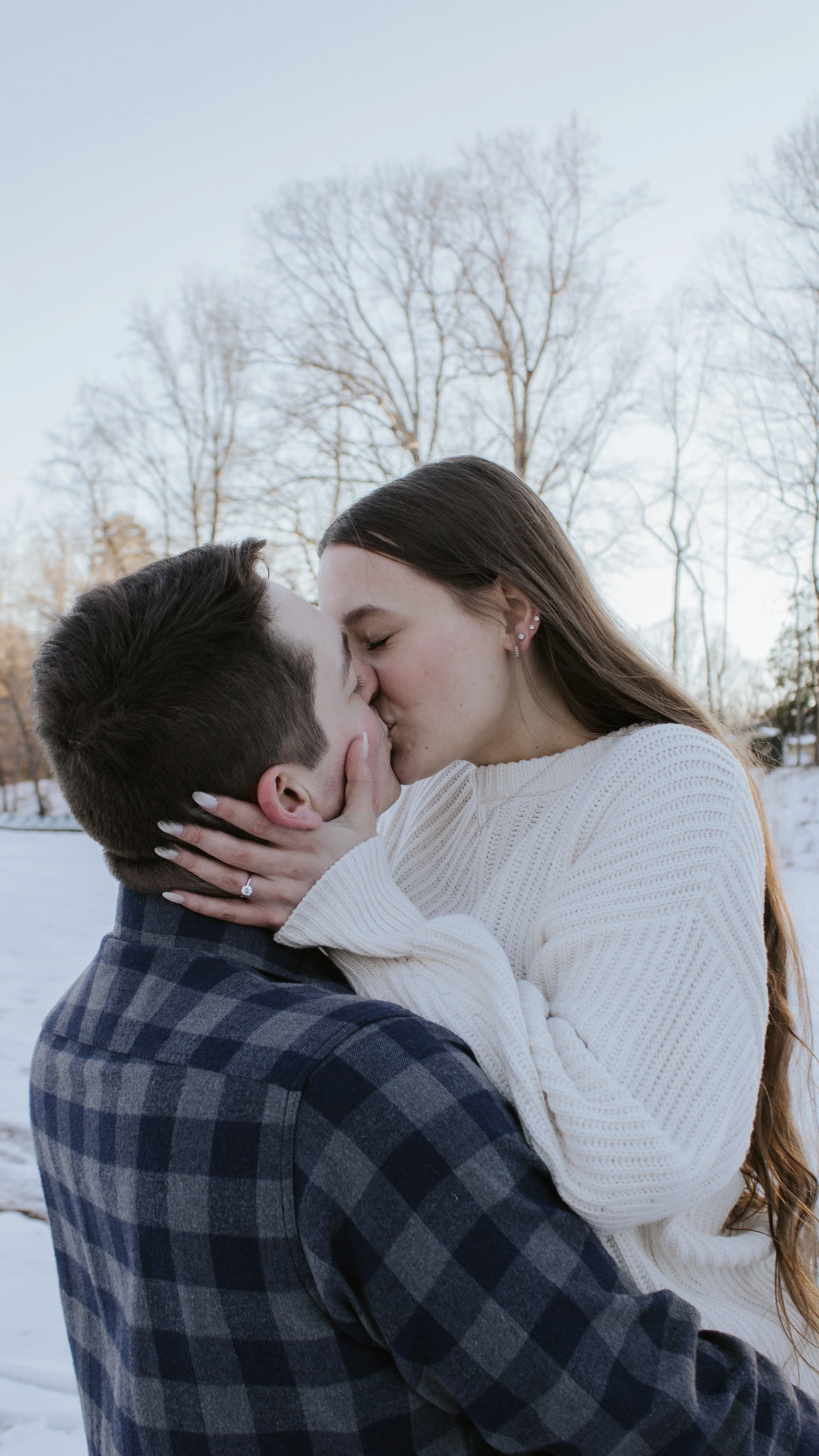 A young couple sharing a kiss outdoors in a snowy landscape on a winter day.