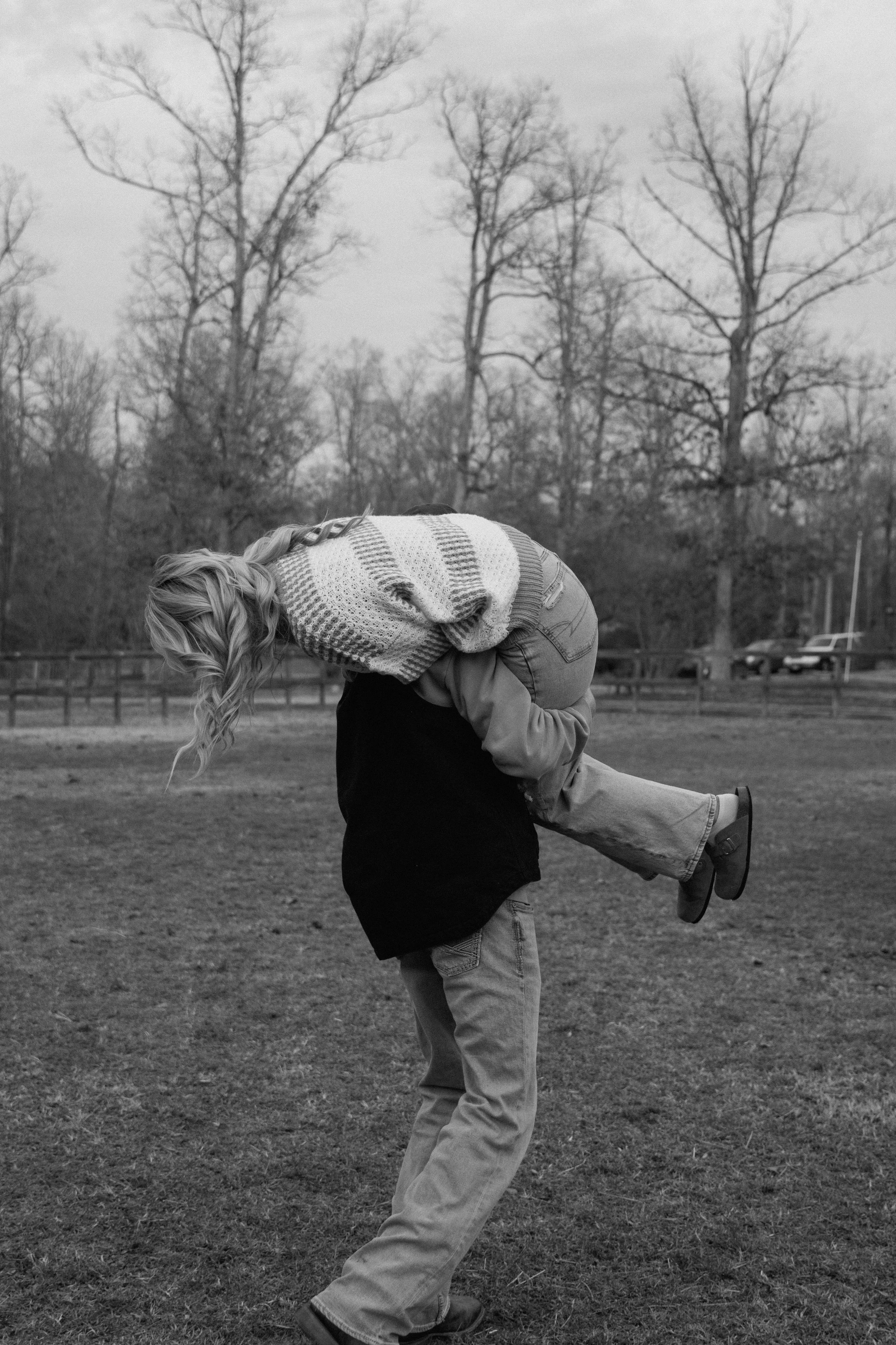 A person carrying another person on their back in an outdoor park with leafless trees.
