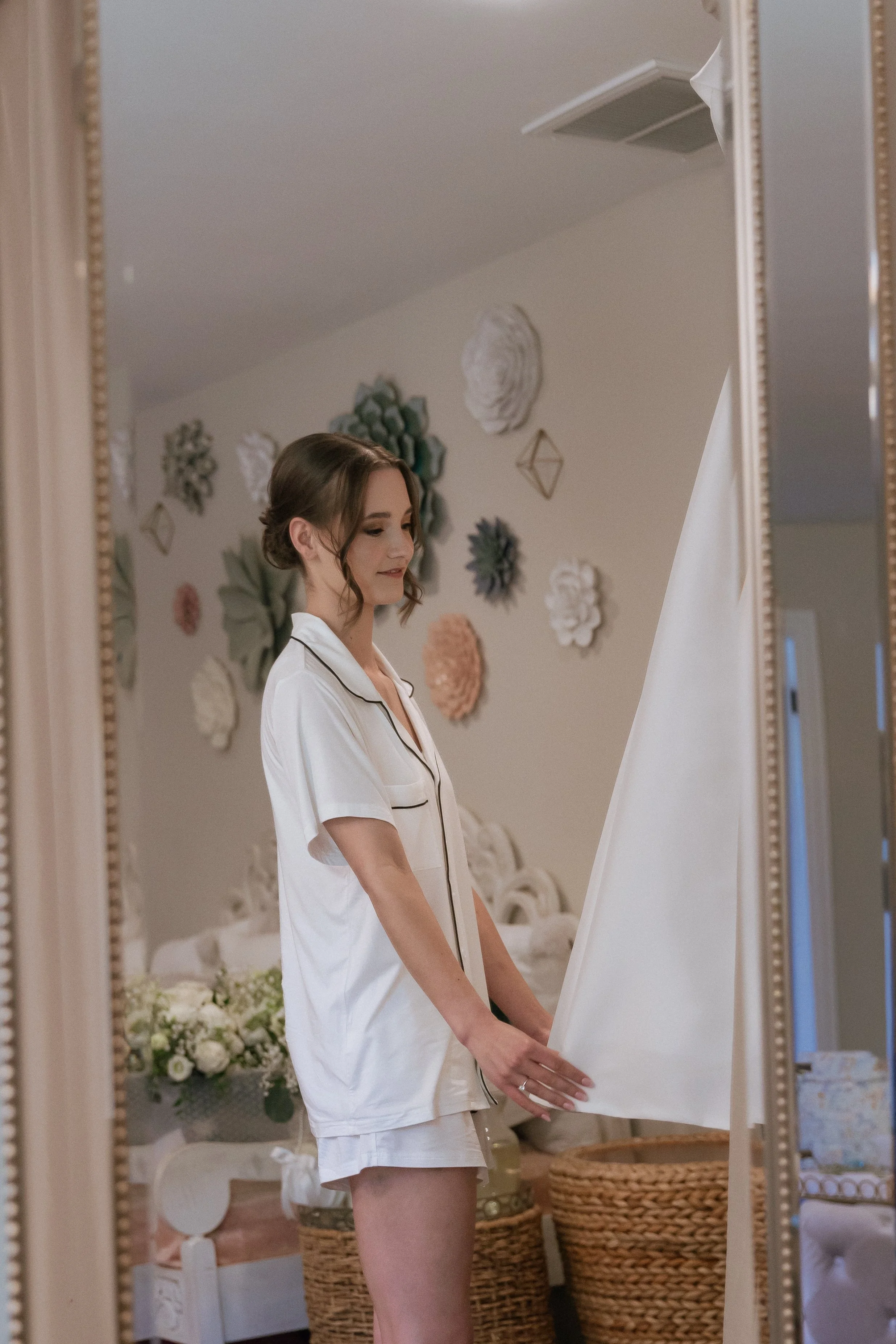 A photo of a reflection in a gold framed mirror of the bride admiring her wedding dress in white pajamas before putting it on.