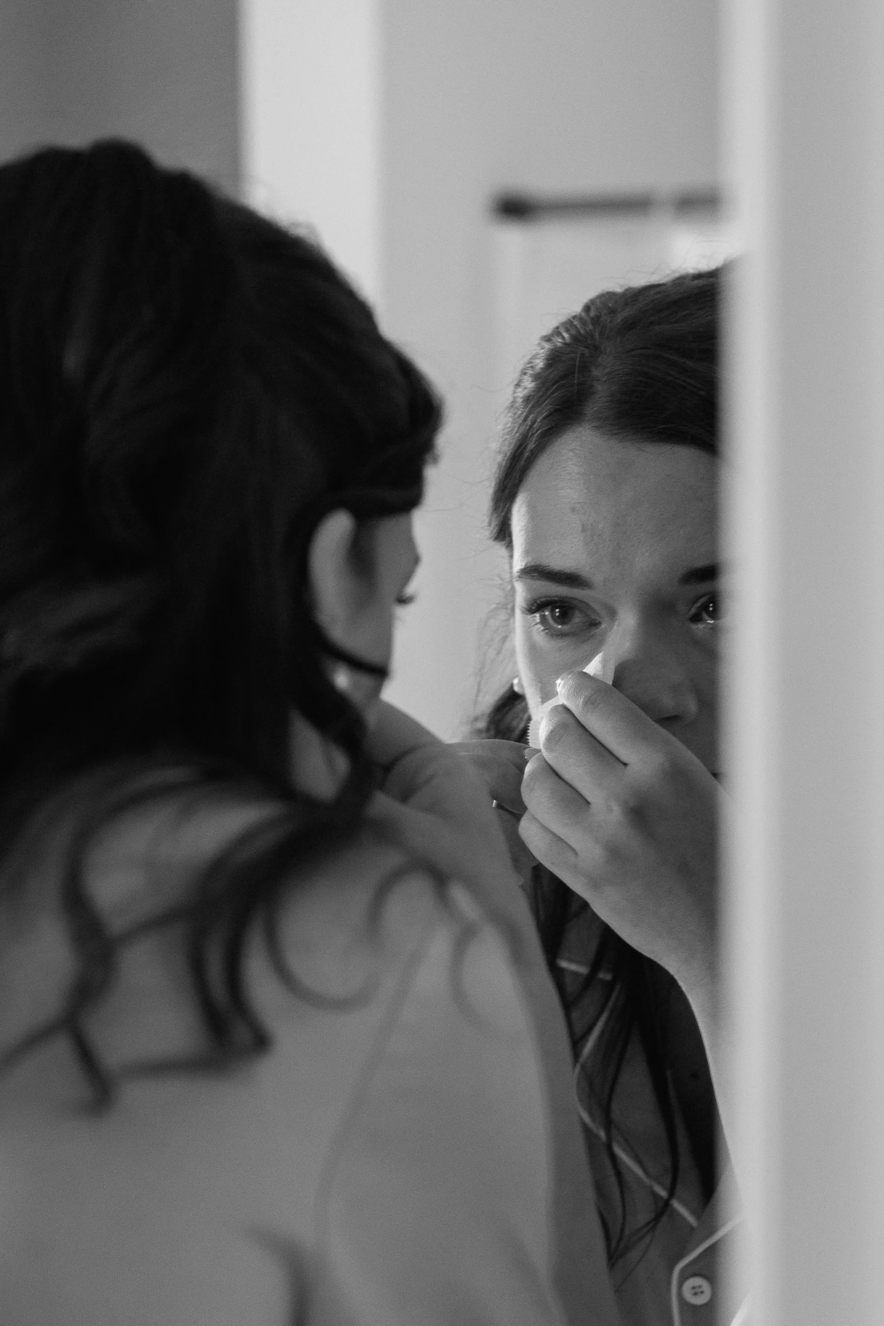 A woman looking into a mirror, fixing her lipstick or makeup.