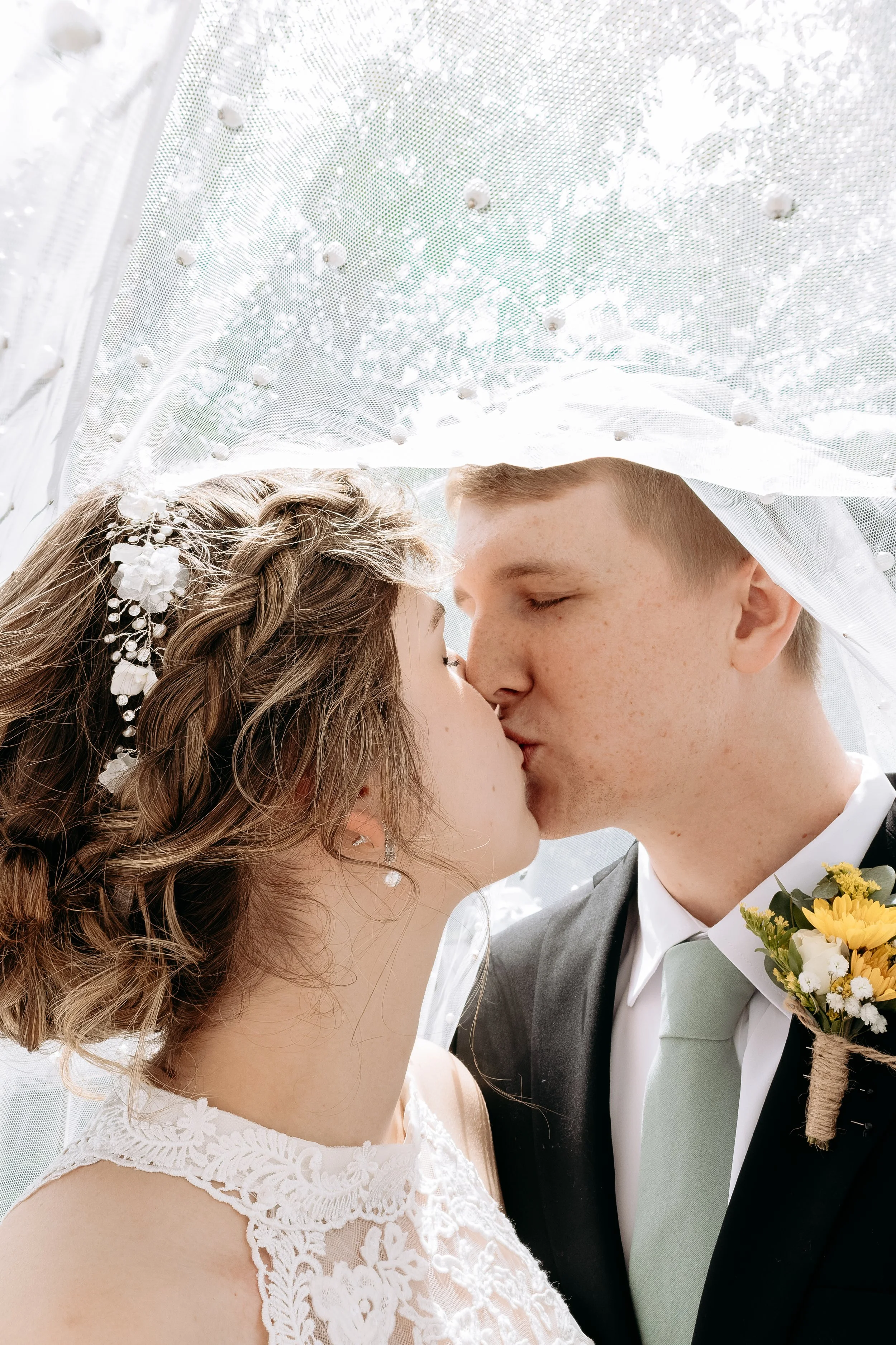 Bride and groom kissing under a lace veil during wedding.