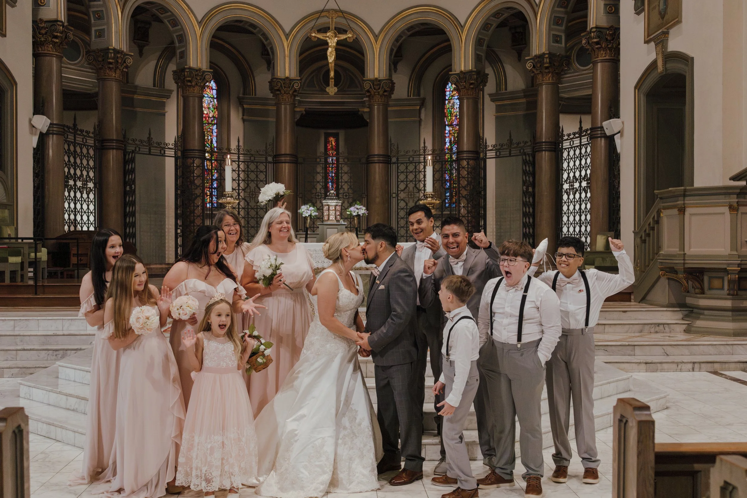 A wedding ceremony inside a church with the newlywed couple kissing, surrounded by family and friends celebrating.