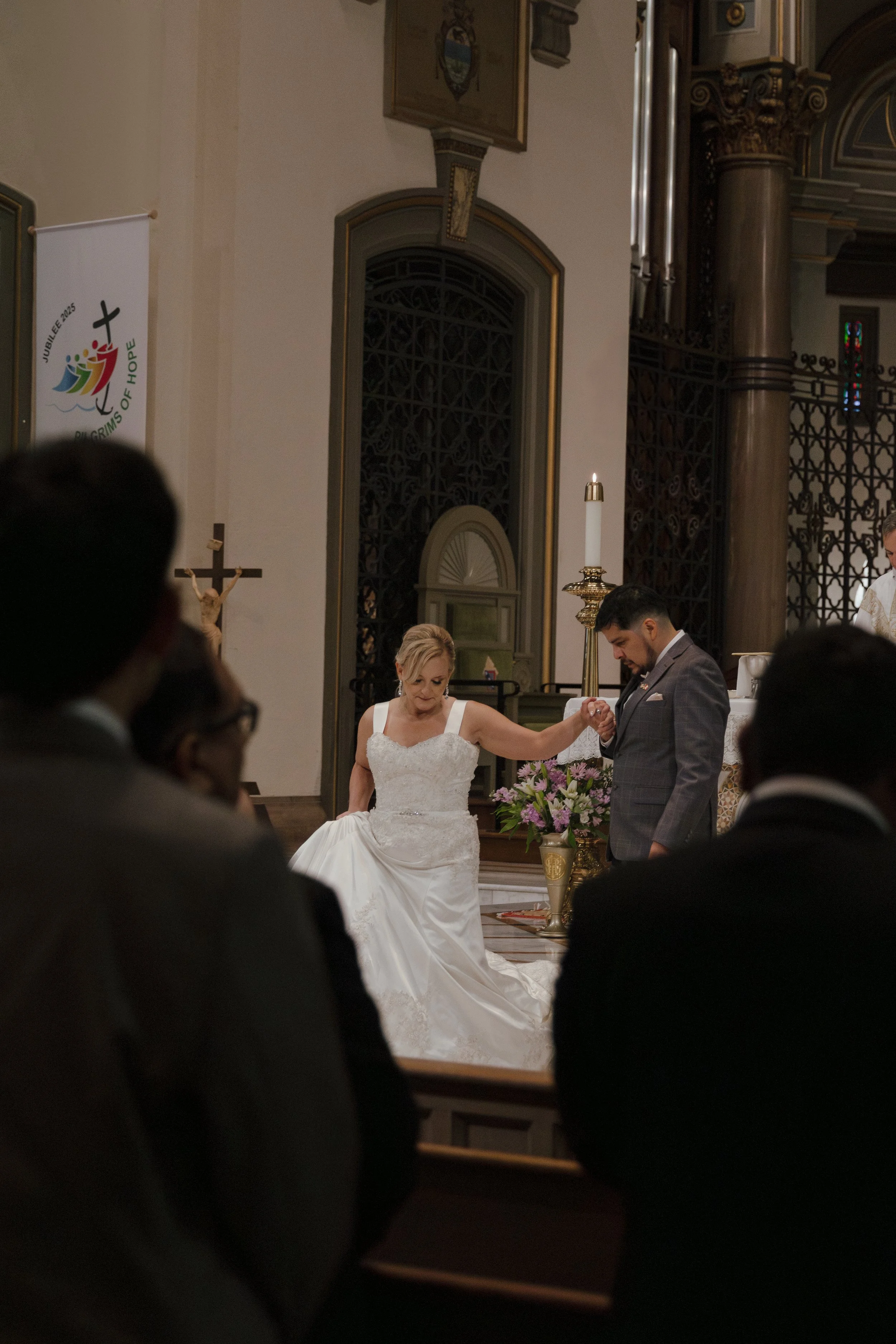 A bride and groom exchanging vows during a wedding ceremony inside a church, with guests seated in the foreground.