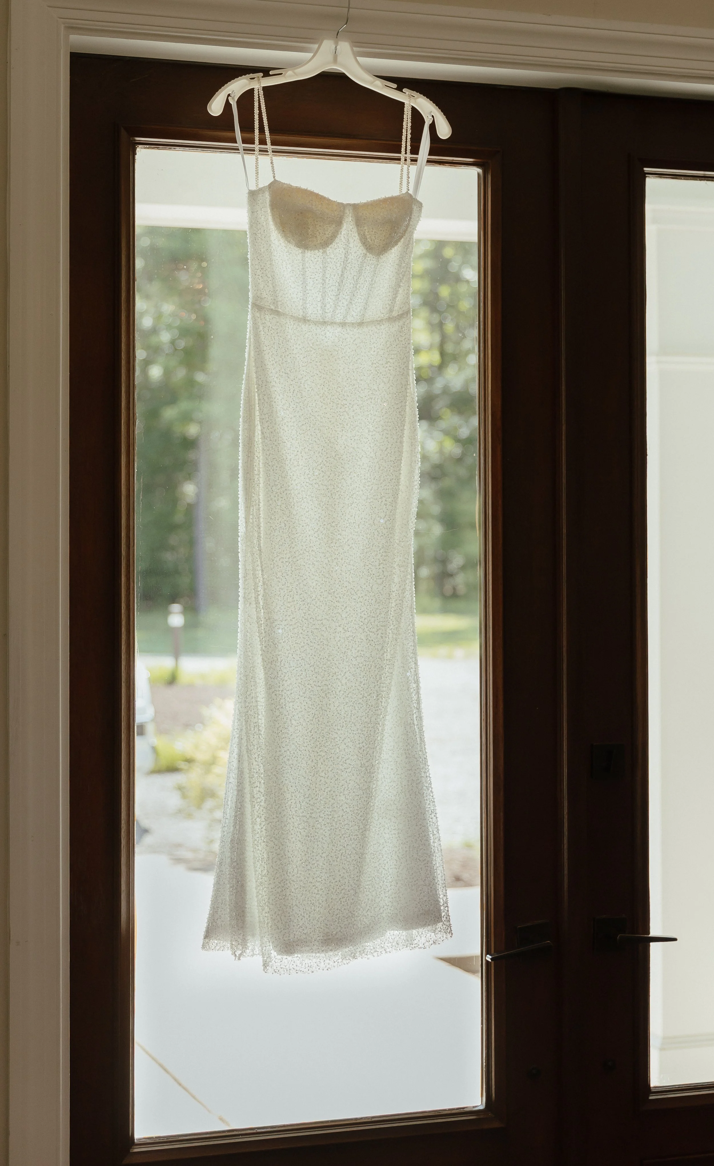 A detail photo of a sequin white dress hanging against a wooden glass door.