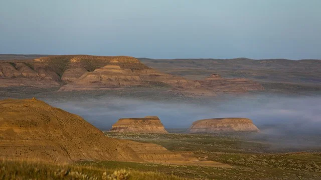 Misty landscape with flat-topped hills and desert terrain under a clear sky.