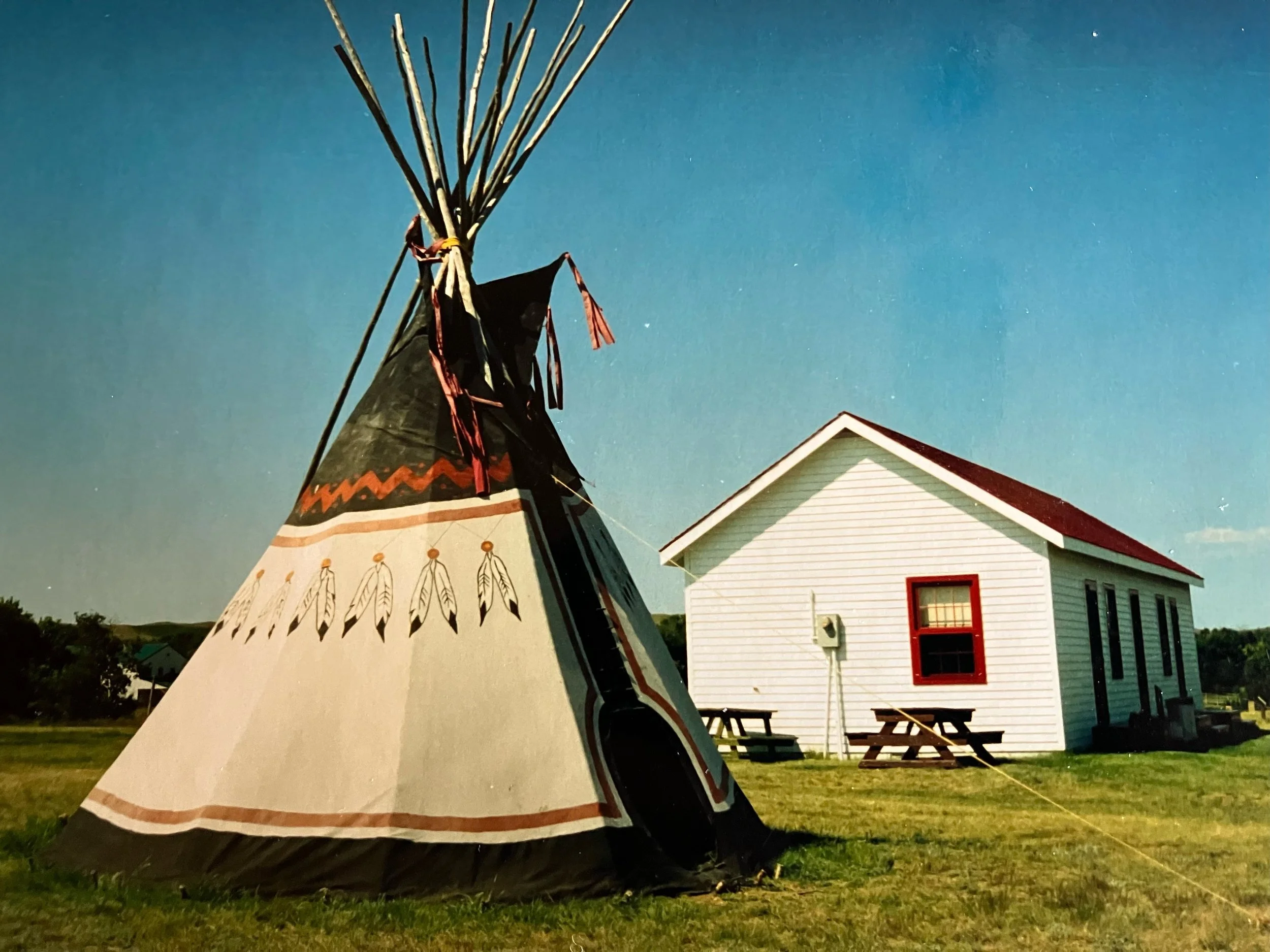A group of people riding horses and covered wagons on a dirt path in a grassy field, reminiscent of a pioneer journey.