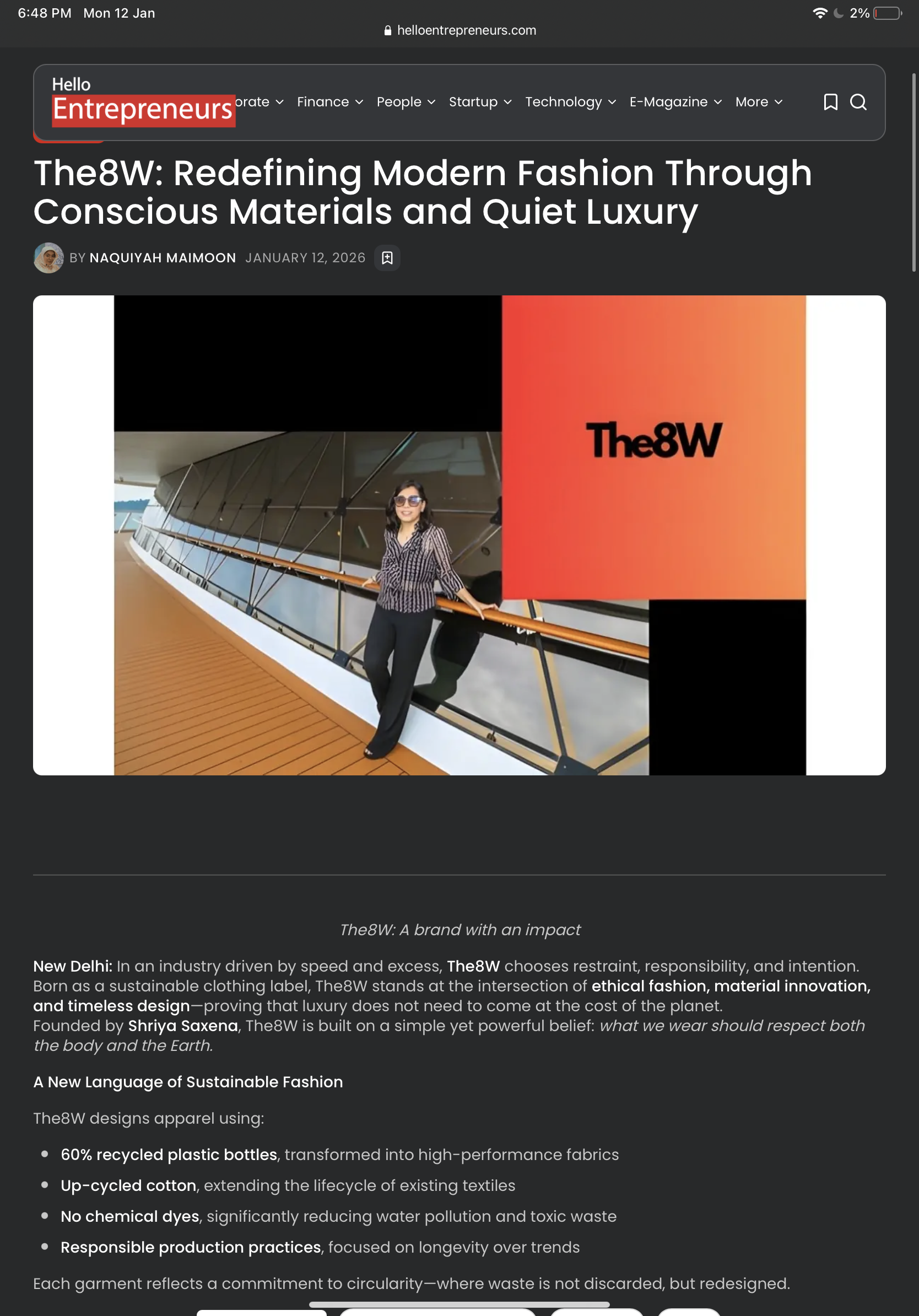 A woman standing on a balcony with a modern building in the background. She is wearing sunglasses, a black and white striped top, and black pants. The webpage header displays the title 'The8W: Redefining Modern Fashion Through Conscious Materials and Quiet Luxury' from helloentrepreneurs.com.