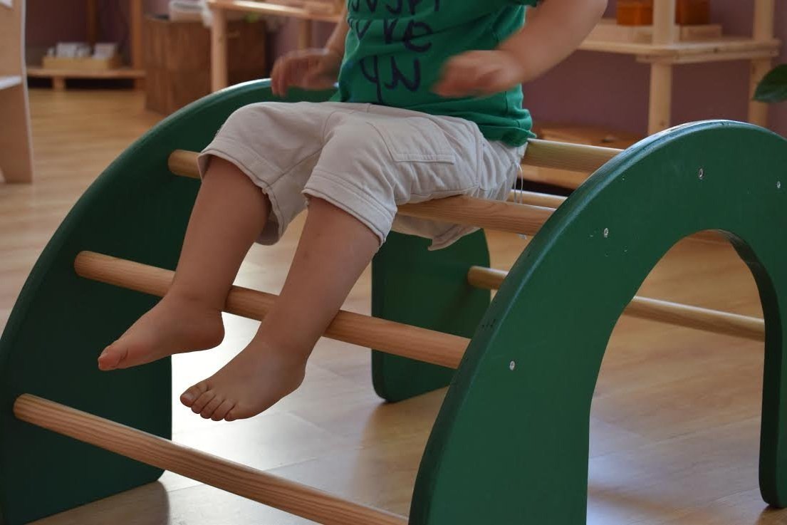 Niño sentado en una estructura de juego de madera en un ambiente interior.