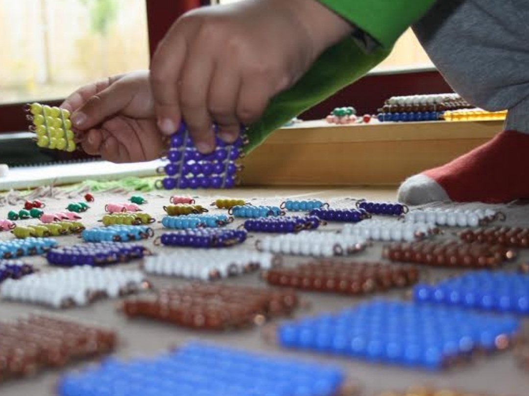 Niño trabajando con cuentas de colores Montessori en una actividad de aprendizaje llamada Decanomio.