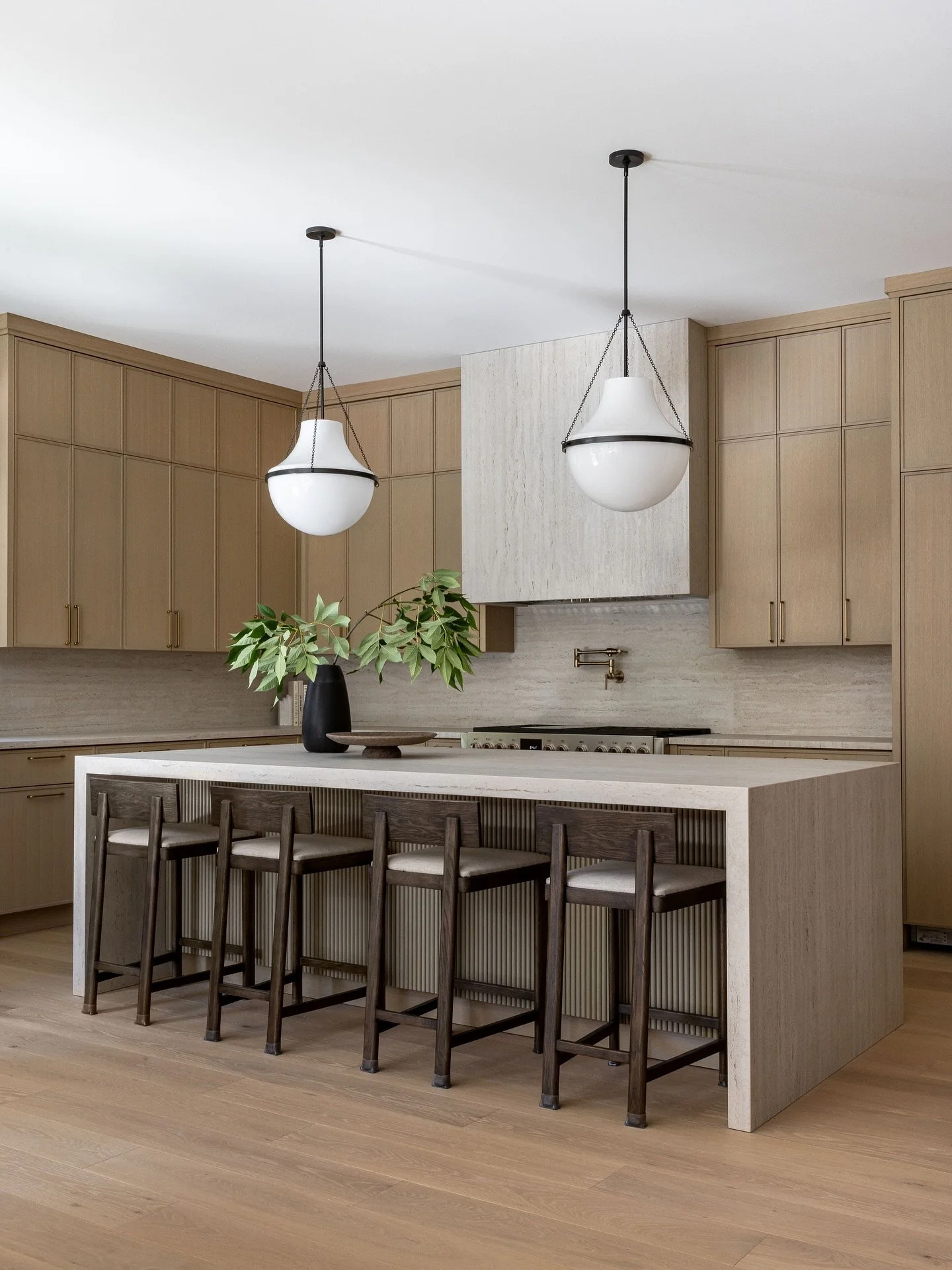 Our clients envisioned a Japandi-inspired, minimalist home with a touch of traditional charm. In the kitchen, we brought that vision to life with &frac12;&rdquo; slim Shaker cabinets and a travertine-like stone hood. The schoolhouse pendants nod to t