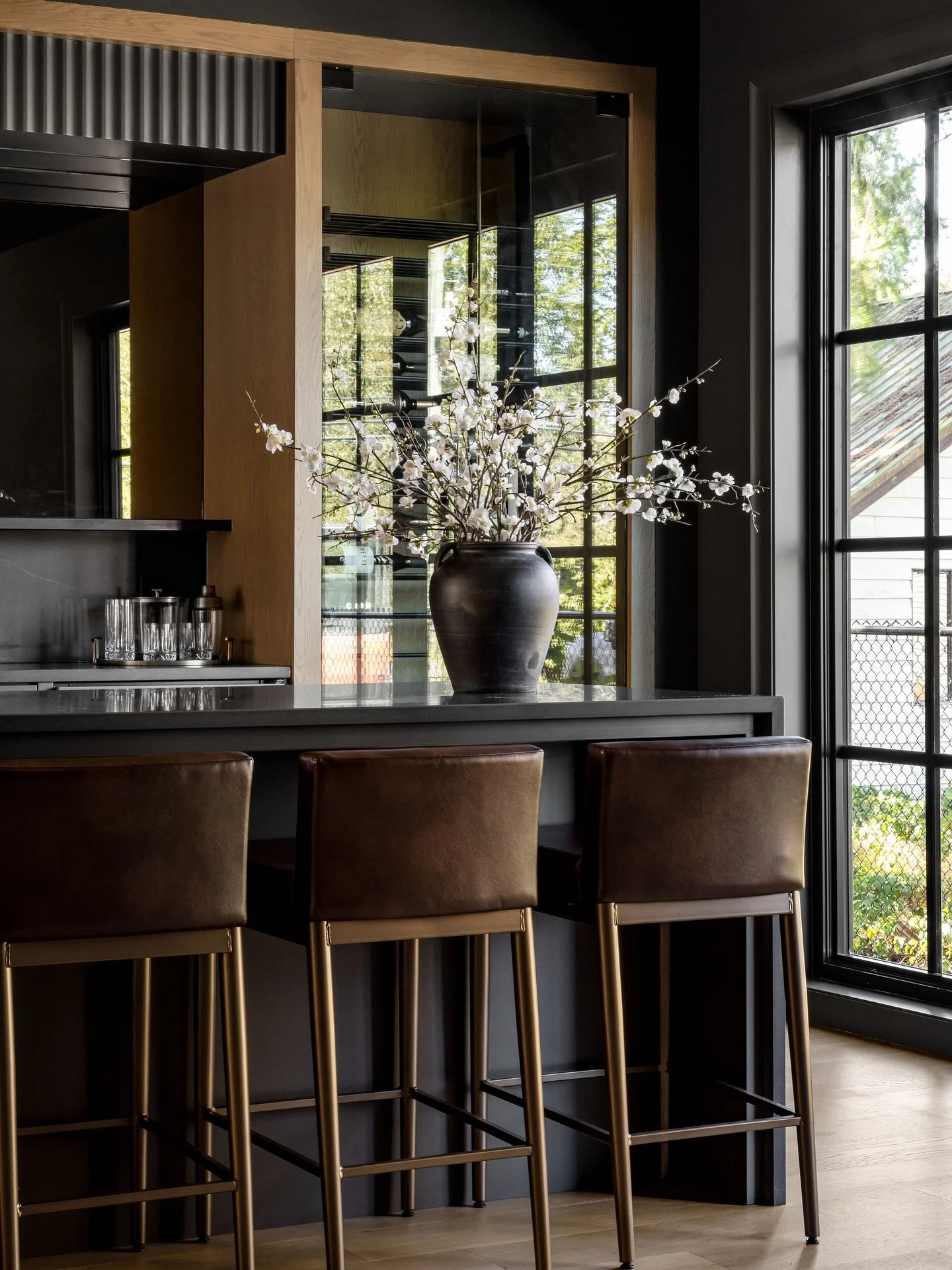 Meet the moody bar of our dreams! With smoked glass detailing, walls drenched in Sherwin Williams&rsquo; Urbane Bronze, and warm natural wood tones, this is the perfect place to pour one up! 🍸 

Interior designer: @centrestagedesign 
Photographer: @
