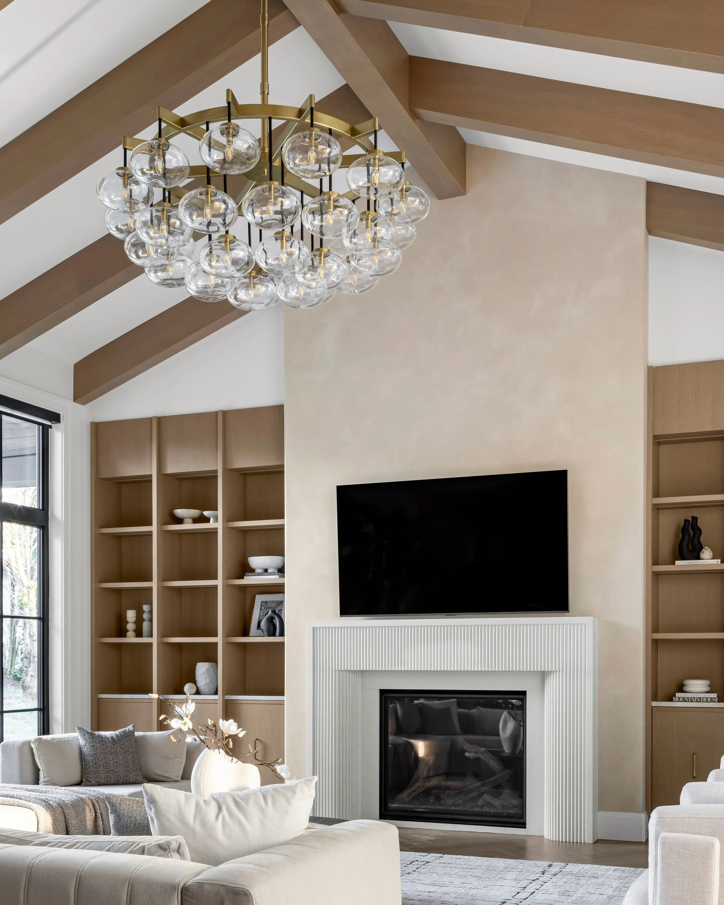 The built ins add so much balance to this great room. Functional storage below, open shelving above, and warm oak tones that bring so much softness to the entire space. Paired with the statement lighting and plaster feature wall, the entire design dr