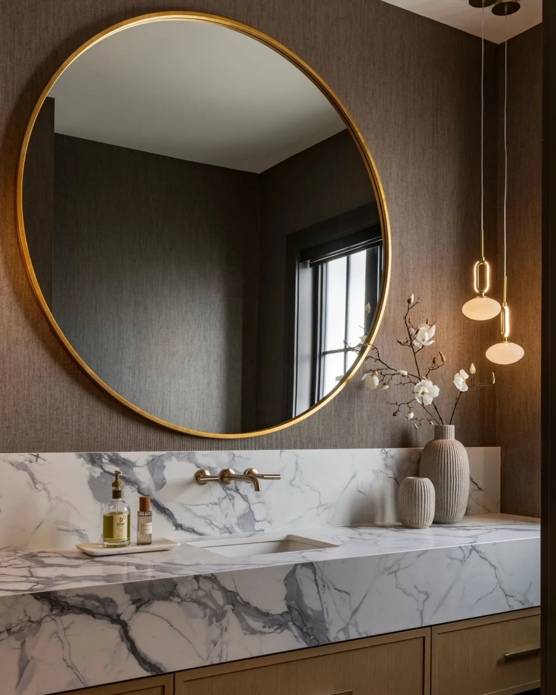 Proof that a powder room can be one of the most memorable spaces in a home! Between the oversized mirror, dramatic veining, and offset pendant lighting layered against textured wraparound wallpaper, this space is designed to make a lasting impression