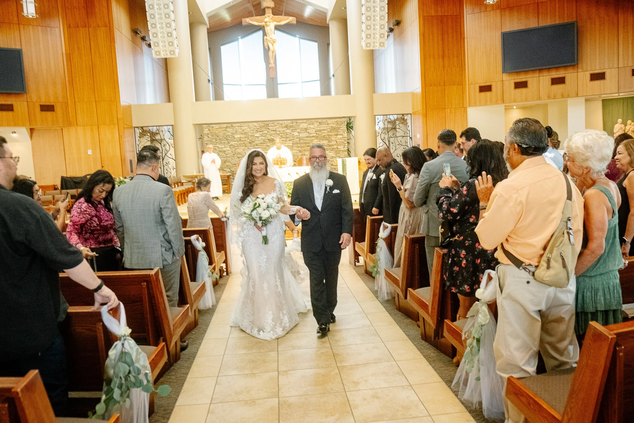 Bride walking down the aisle with her father in a church filled with guests
