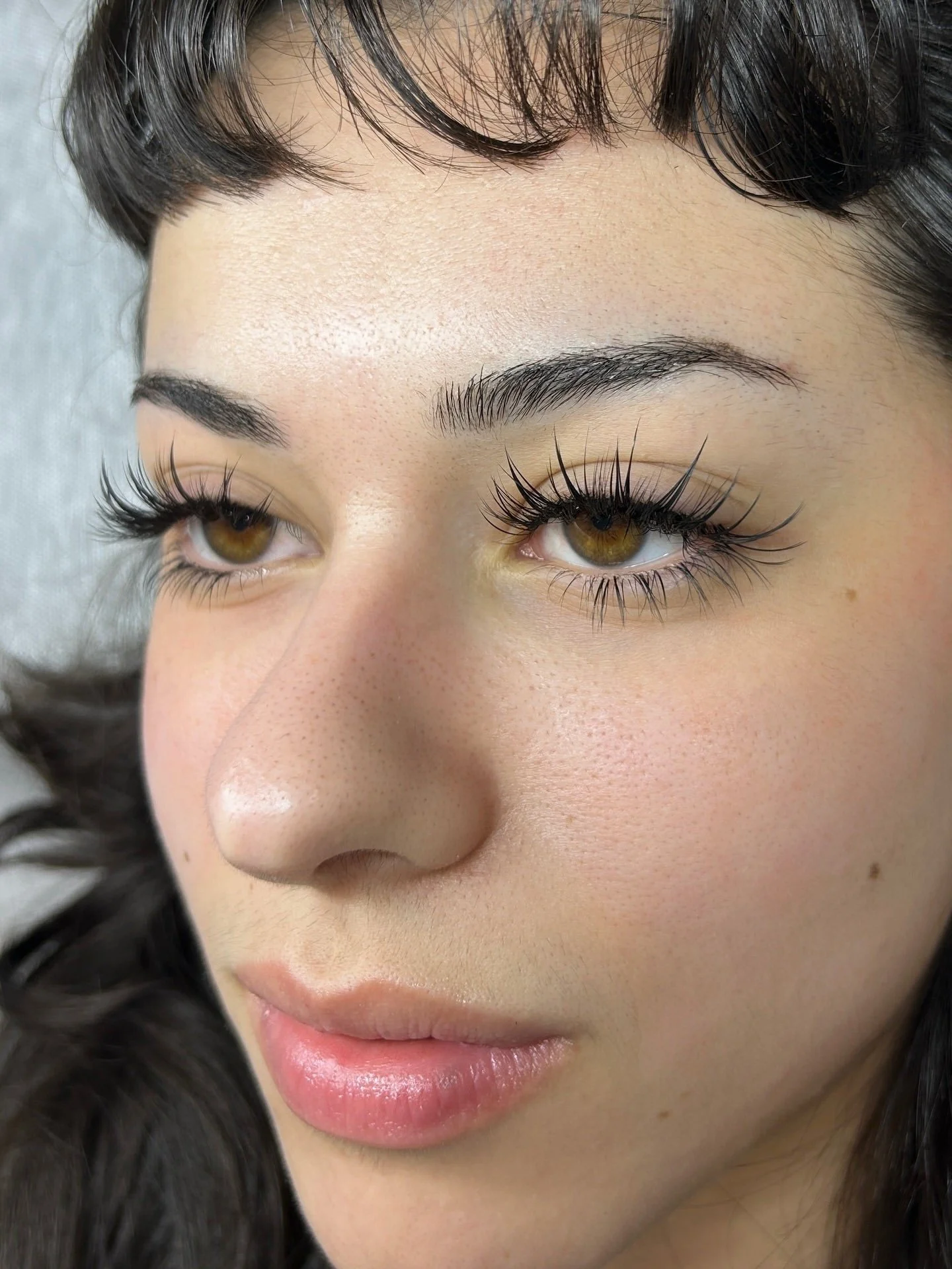 Close-up of a woman’s face highlighting Medusa-style eyelash extensions — dramatic spiky wispy lashes with sharp texture and separated lash spikes. Brown eyes, soft makeup, arched brows, and dark hair. Focus on the detailed lash design around the eye