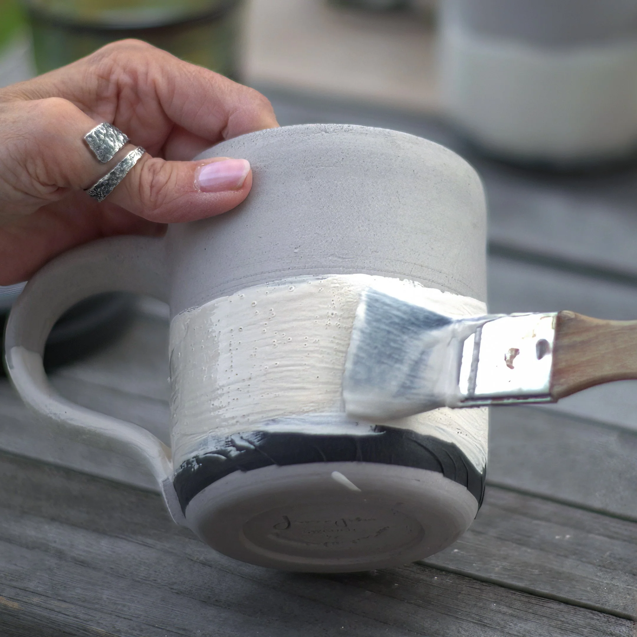Person trägt weißen Lack auf einen grauen Keramiktassen auf Holzoberfläche.