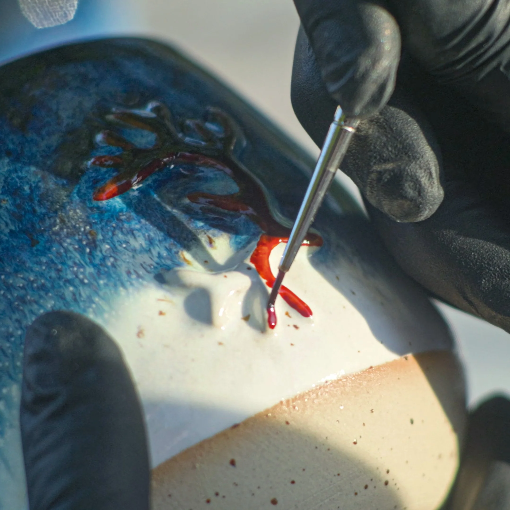 Ein Künstler bemalt eine Skulptur, die einen Fisch darstellt, mit roter Farbe, während er eine feine Pinselführung macht.