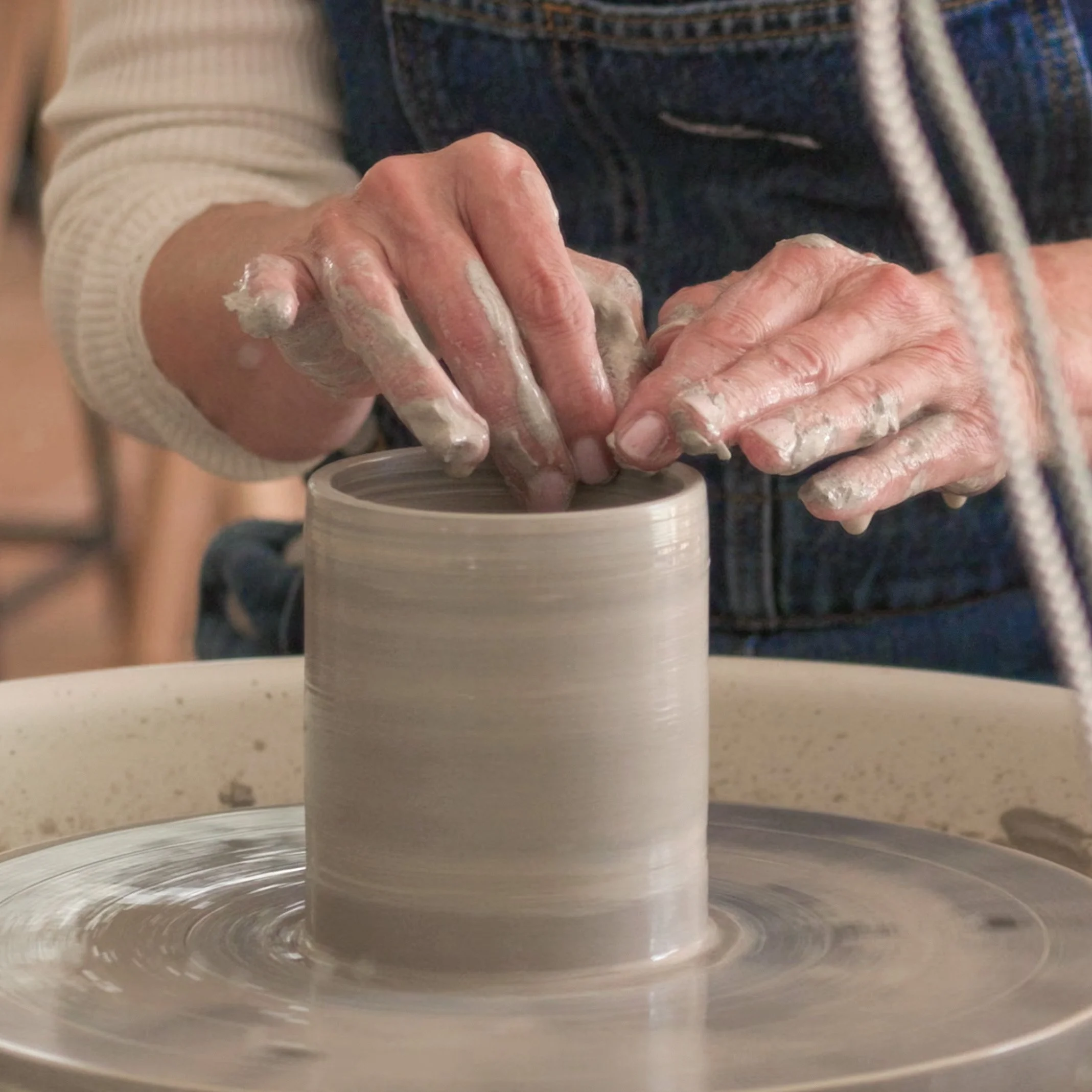 Person beim Töpfern, die Hände formen einen Tonkrug auf einer Drehscheibe.