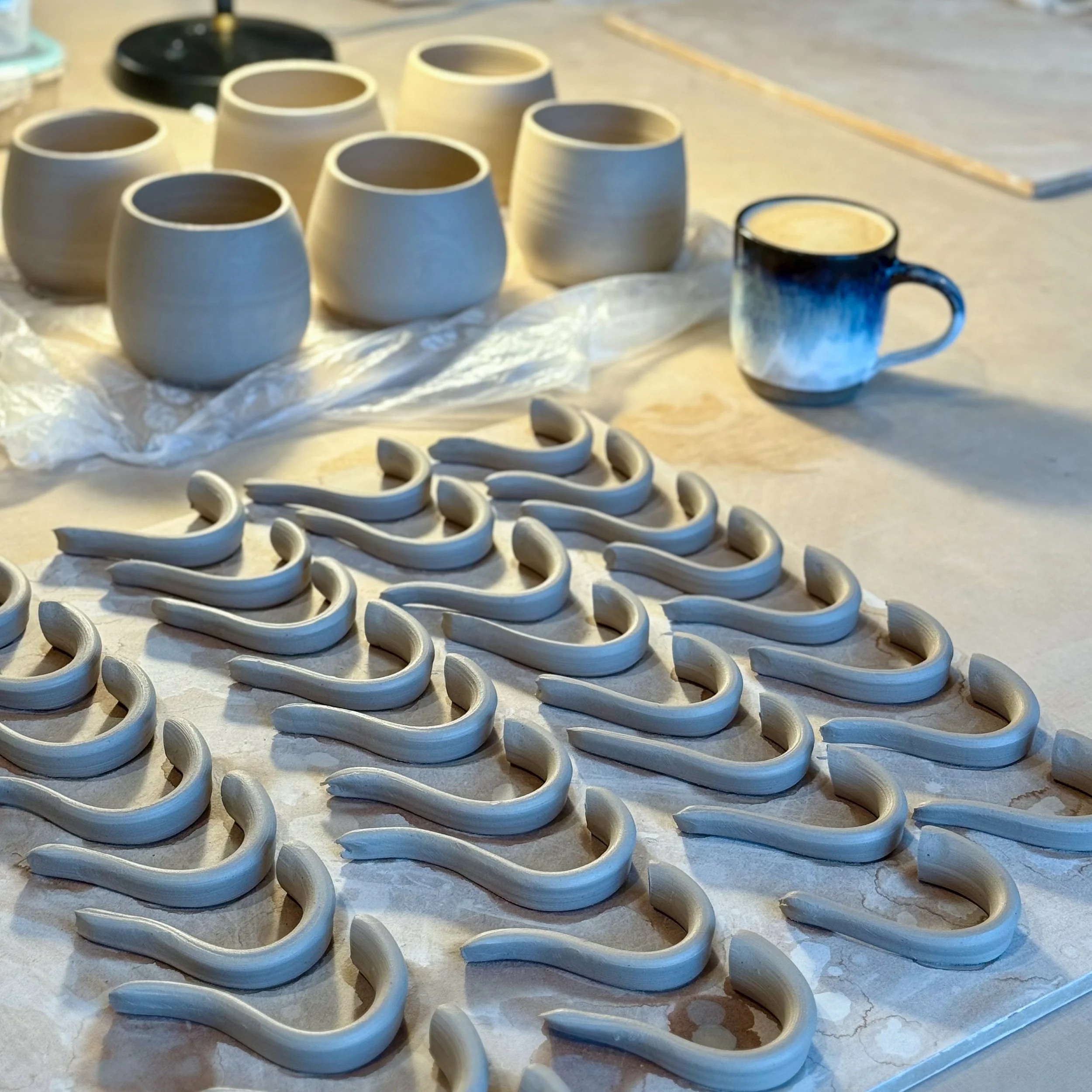 Unvollendete Keramik-Teile, Tassen und Haken, offenbar in einer Keramikwerkstatt hergestellt, auf einer Arbeitsfläche aus Ton oder Tonerde.