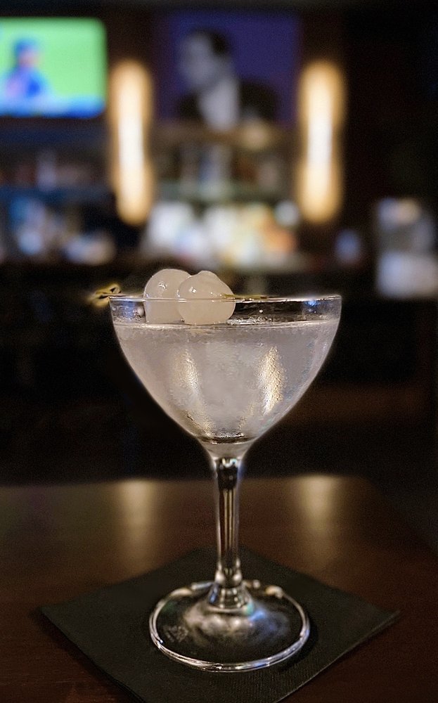 Cocktail glass with clear drink garnished with two cocktail onions, placed on a dark napkin in a dimly lit bar.