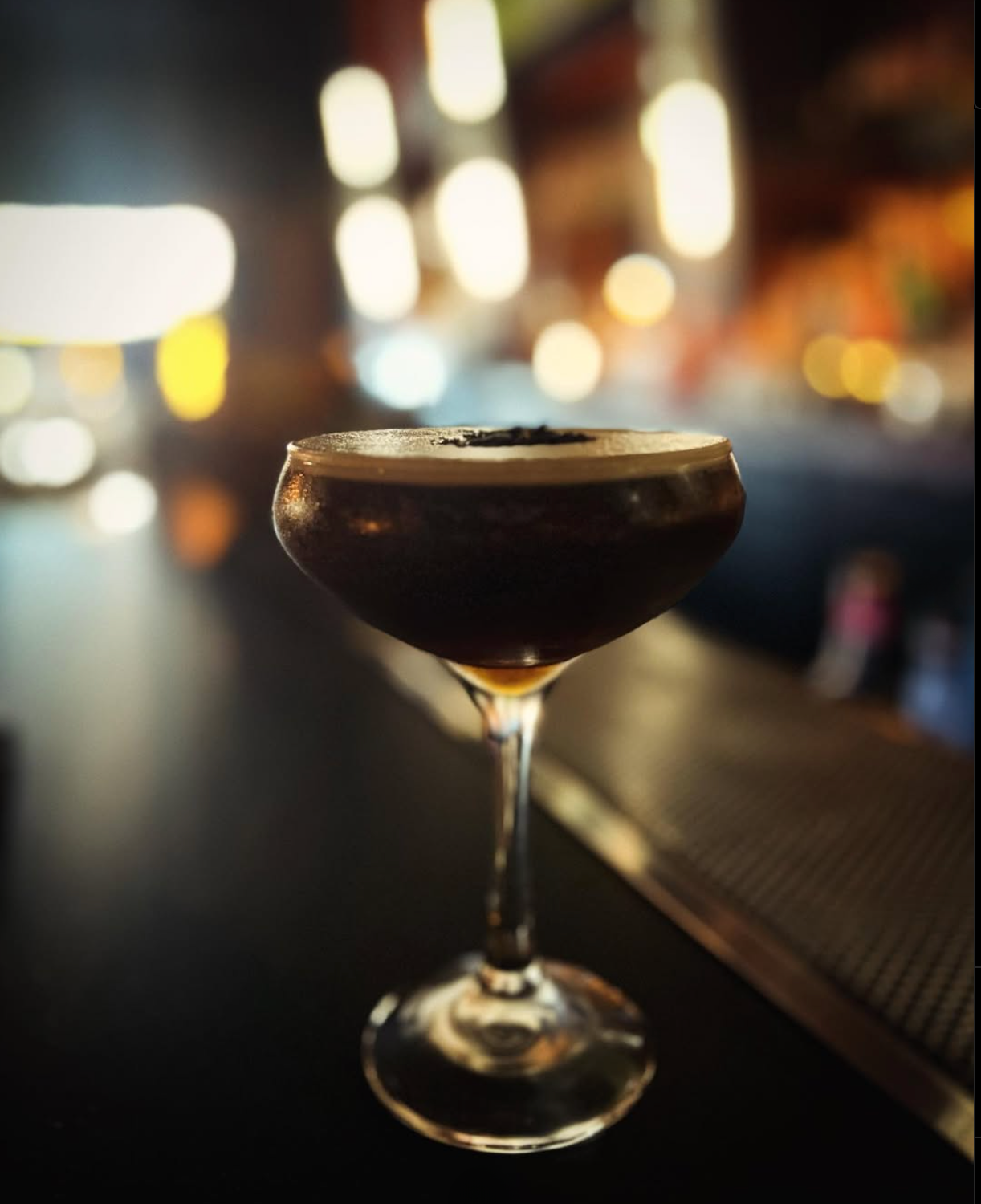 Espresso martini on bar counter with blurred background.