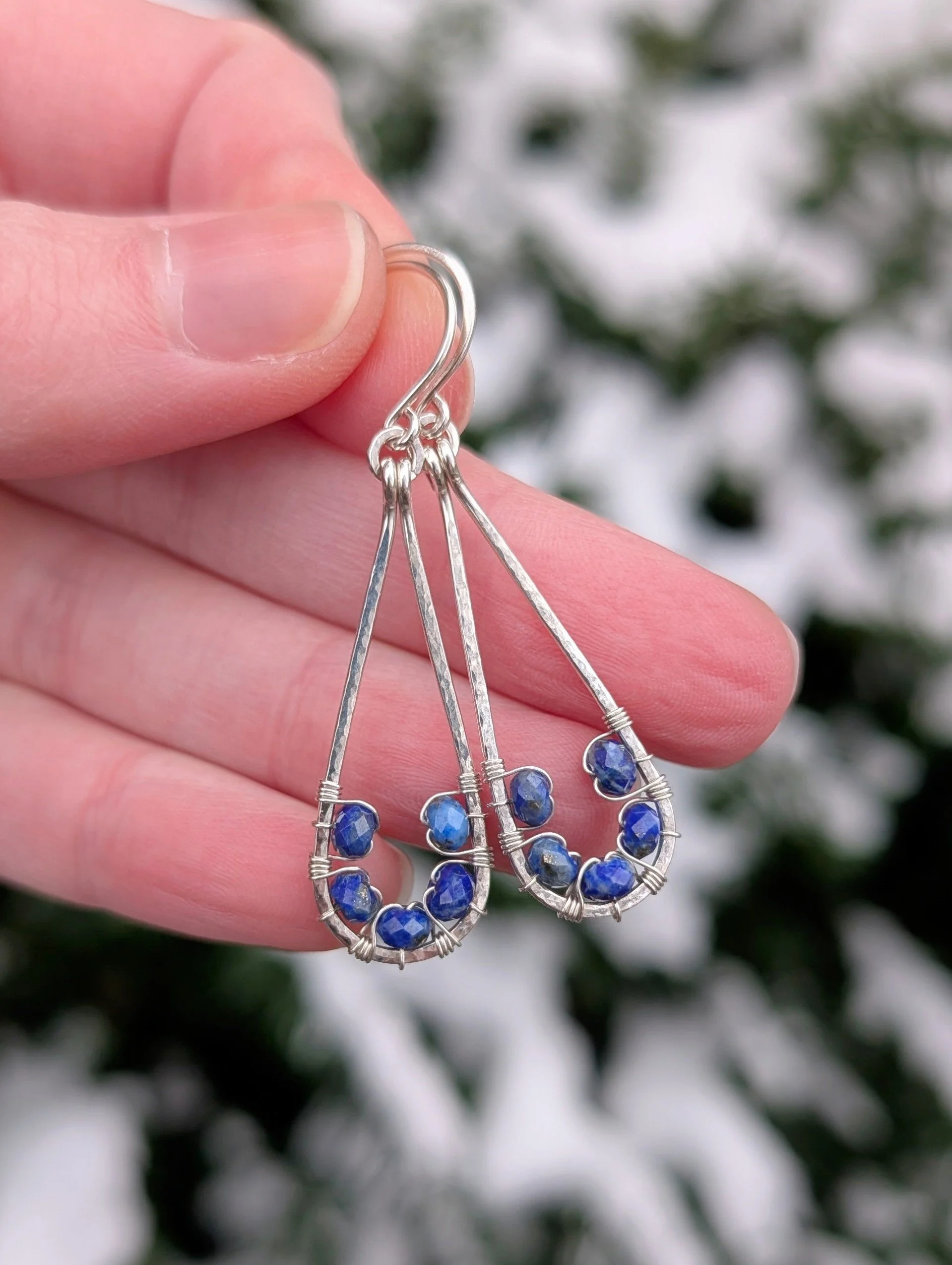 Earrings made with a sterling silver tear drop shaped frame with five small lapis lazuli beads woven on the inside of the frame